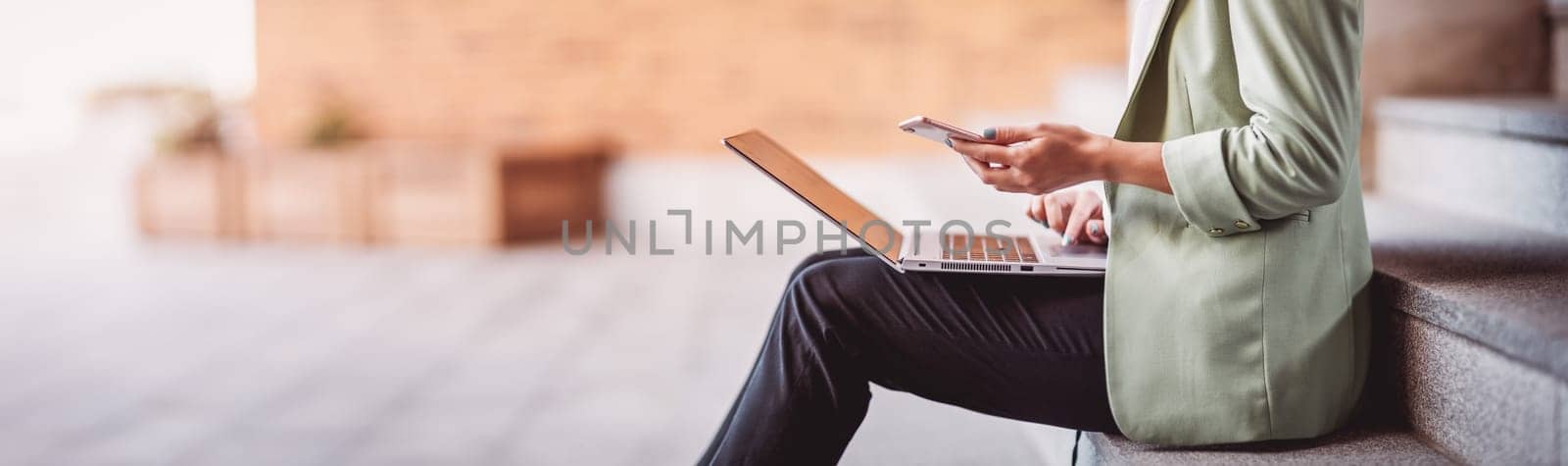 young woman with laptop sitting on the stairs. Person using personal computer outdoors