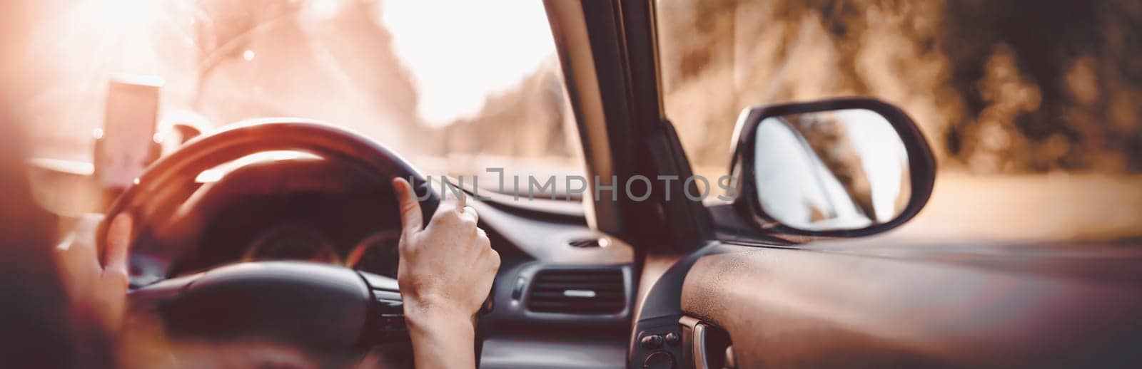 Driver driving a car on asphalt road in summer day at park. Woman at steering wheel