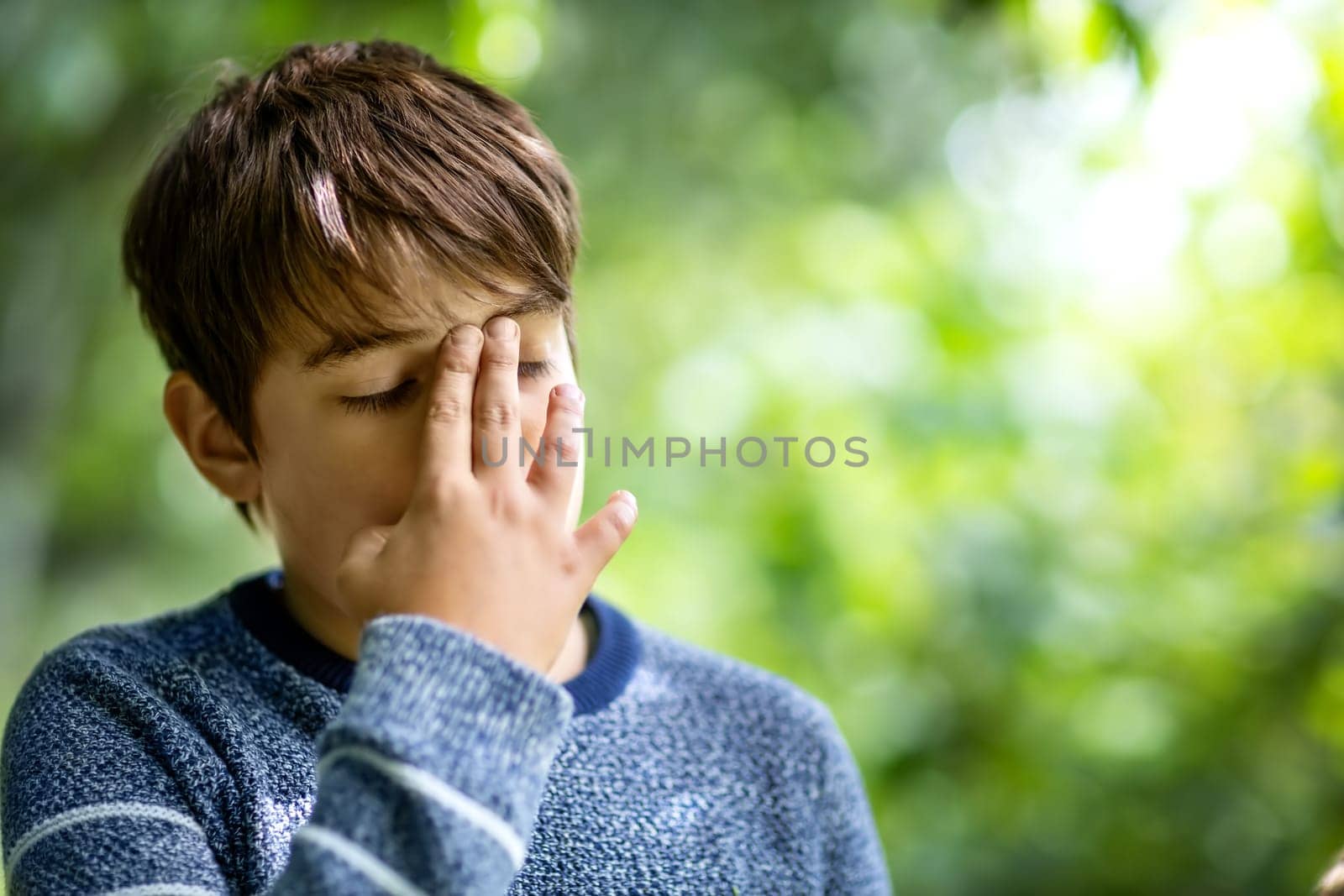 child with headache. Upset young boy outdoors in nature