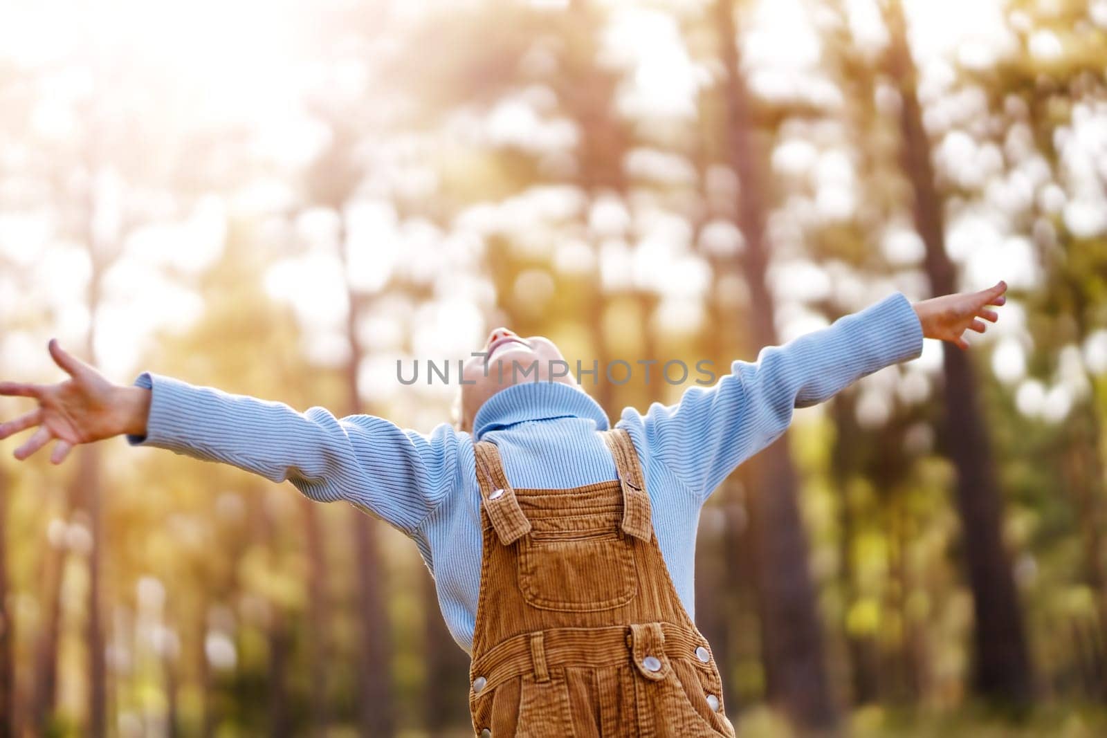 Happy baby boy standing in the forest at sunny summer evening. Smiling child outdoors