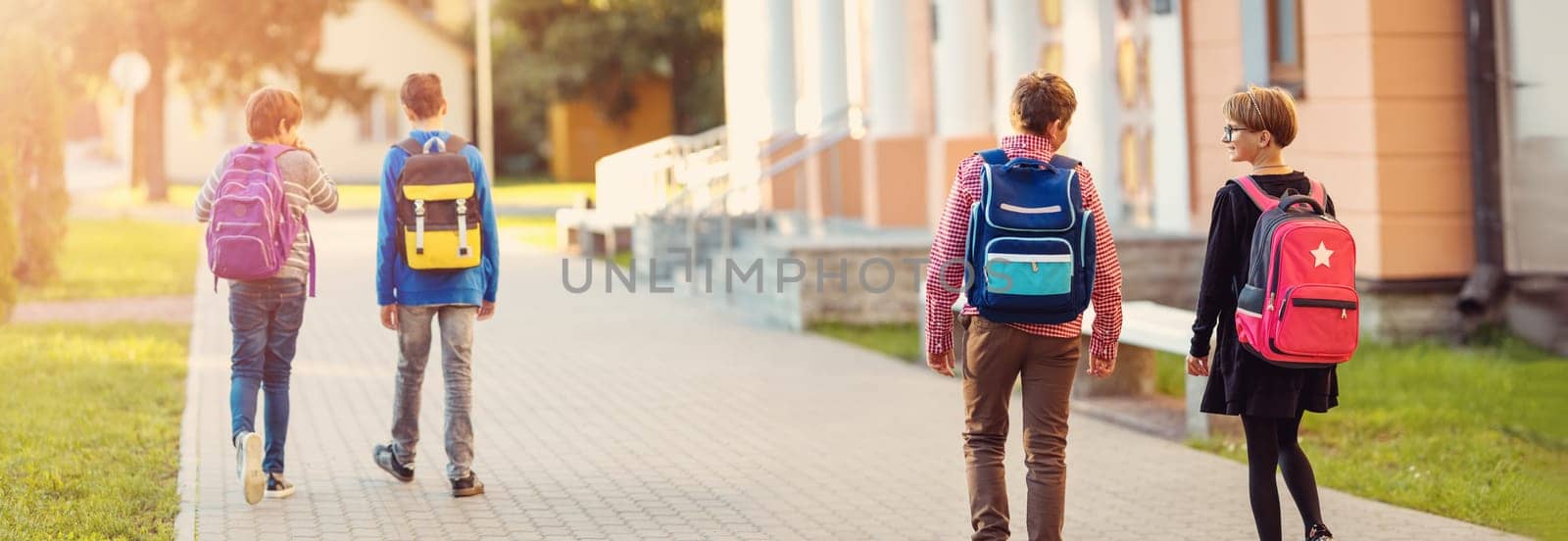 Children with rucksacks standing in the park near school. Pupils with books and backpacks outdoors