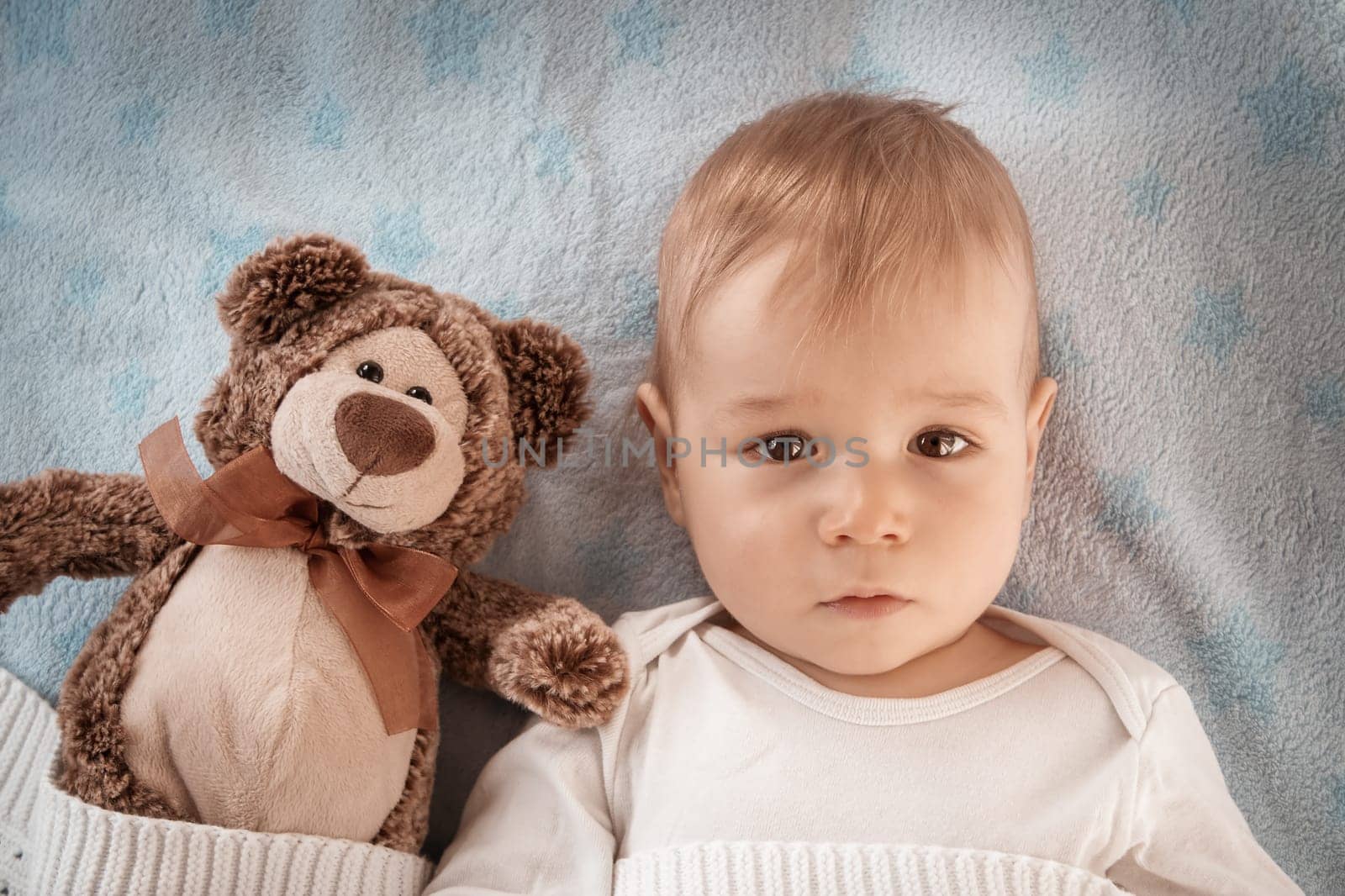 One year old baby lying in bed with a plush teddy bear