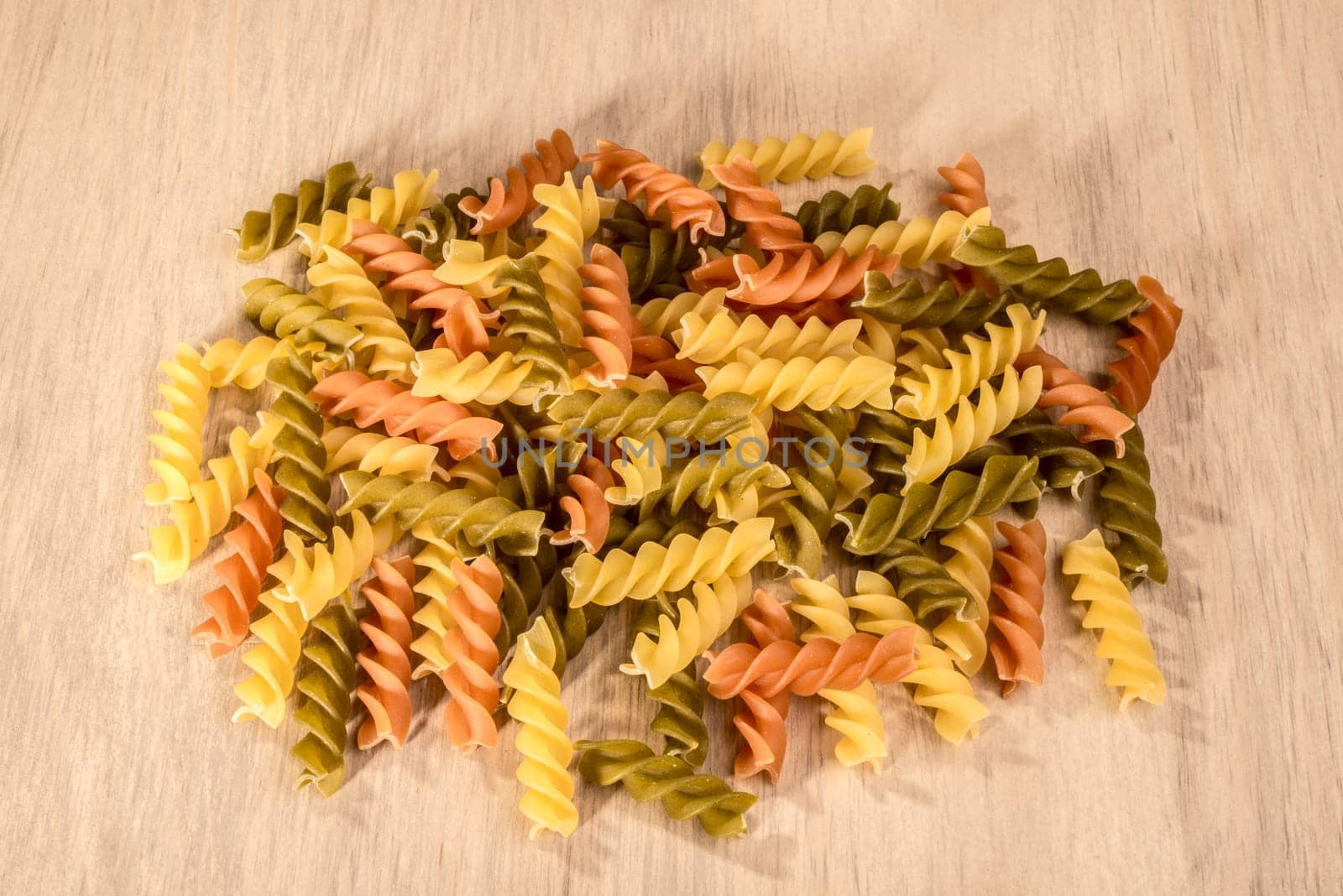 A small heap of three different colours of fussili ly on a wooden table.