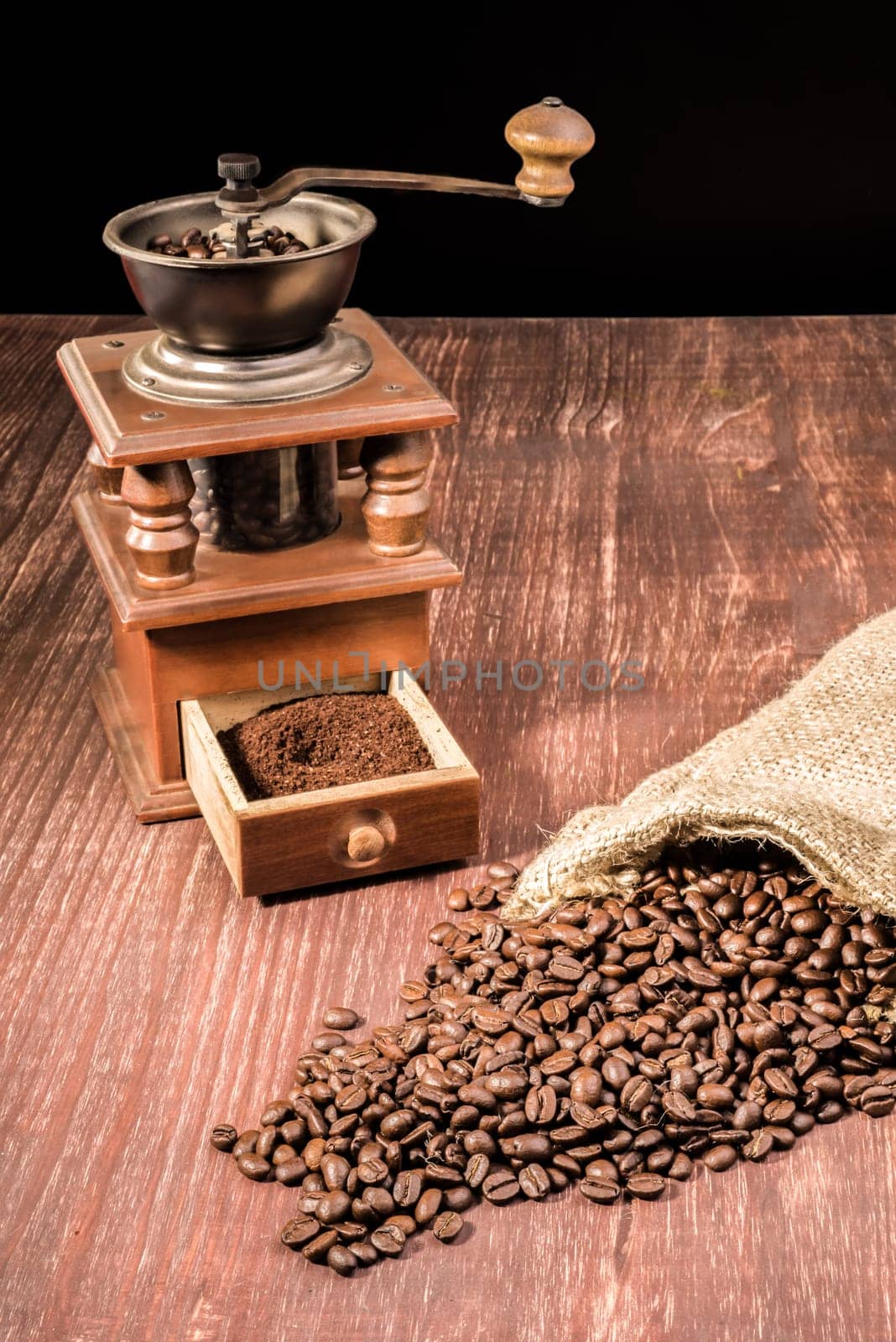 Coffee beans ly spilled from a hessian bag on a wooden table with an old grinder in the back.