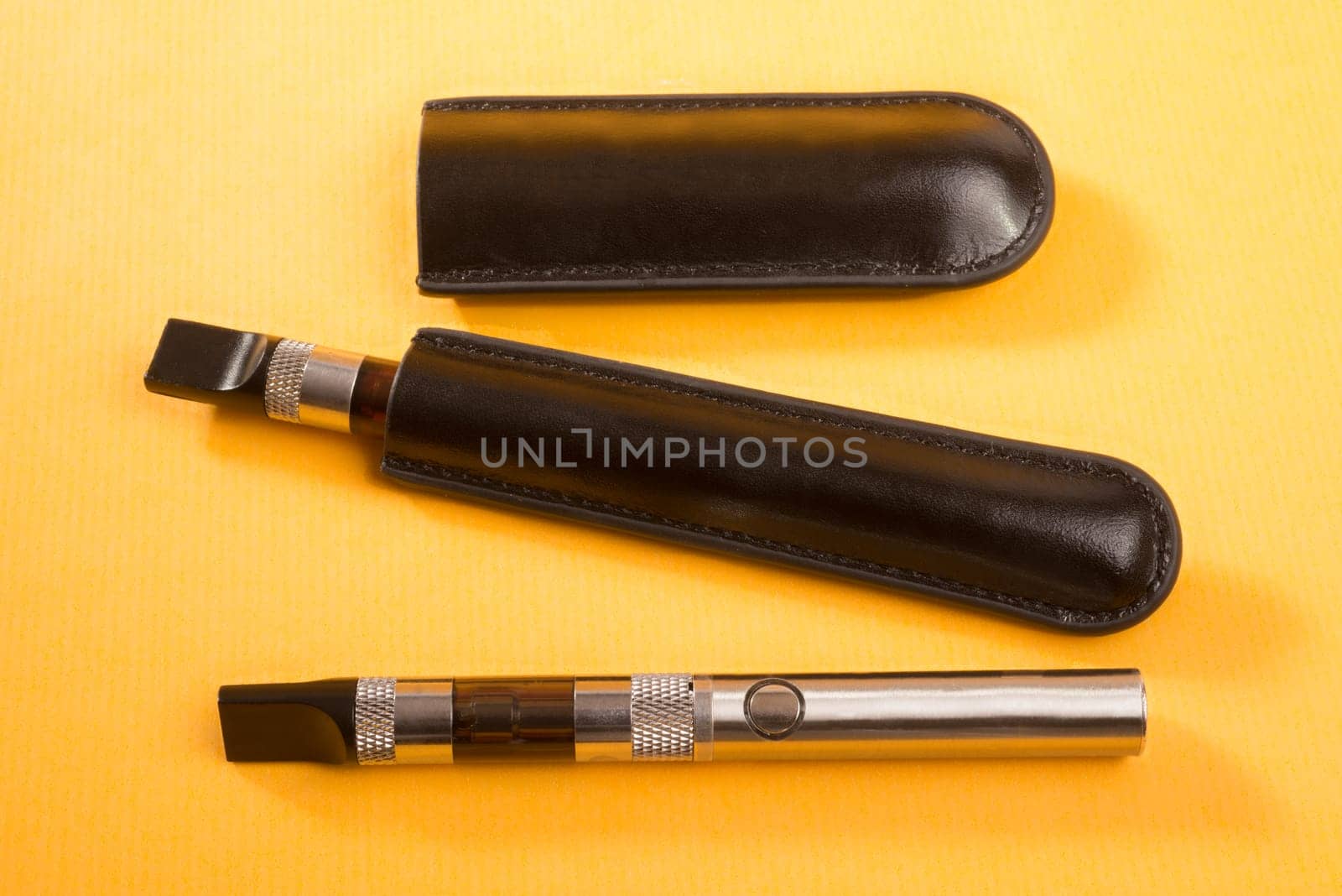 Two electronic cigarettes lie on a yellow background, with one unit still in leather pouch.