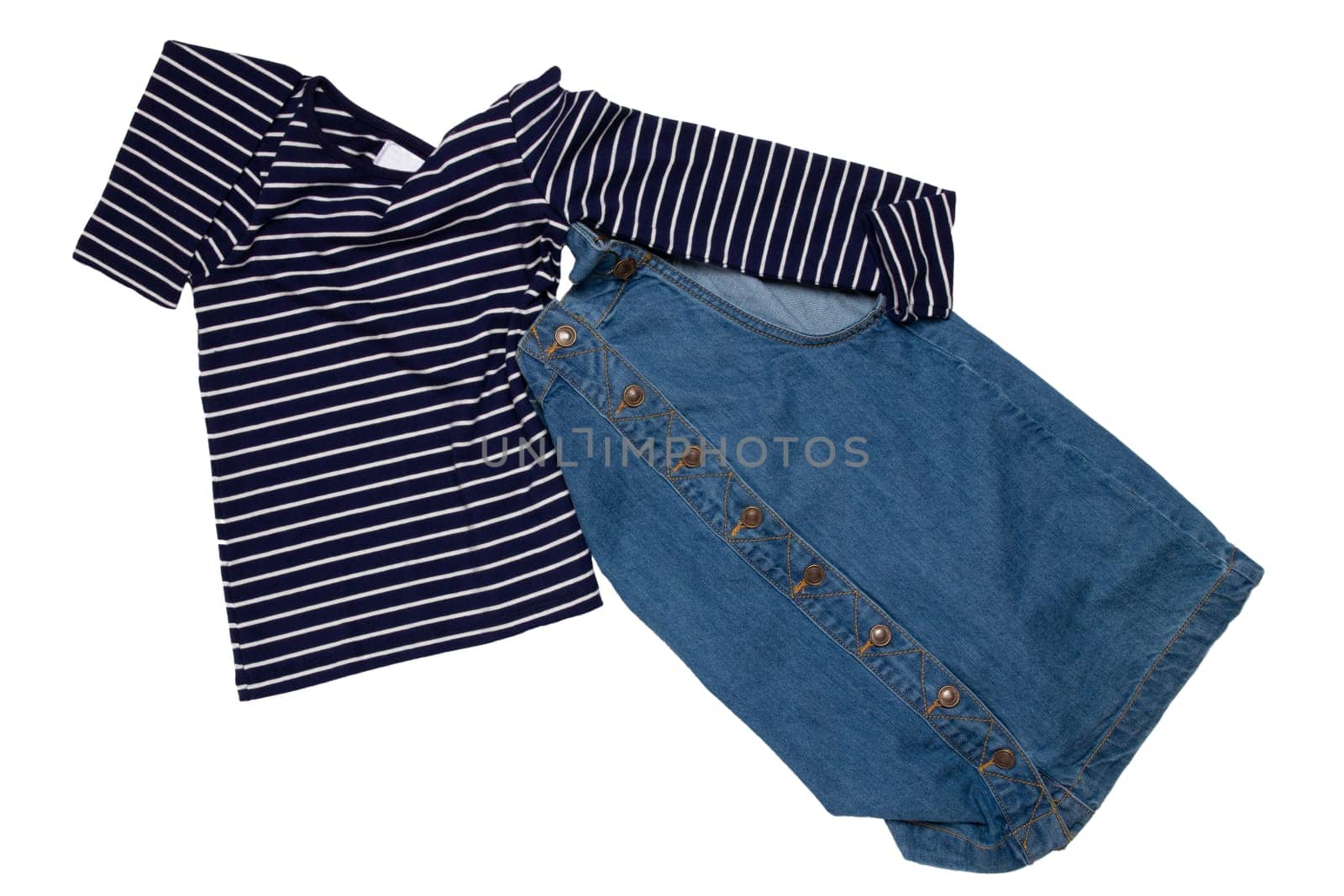 Closeup of folded cute sleeveless blue denim overall dress and striped t-shirt for little child girl isolated on a white background. Jeans fashion for kids.