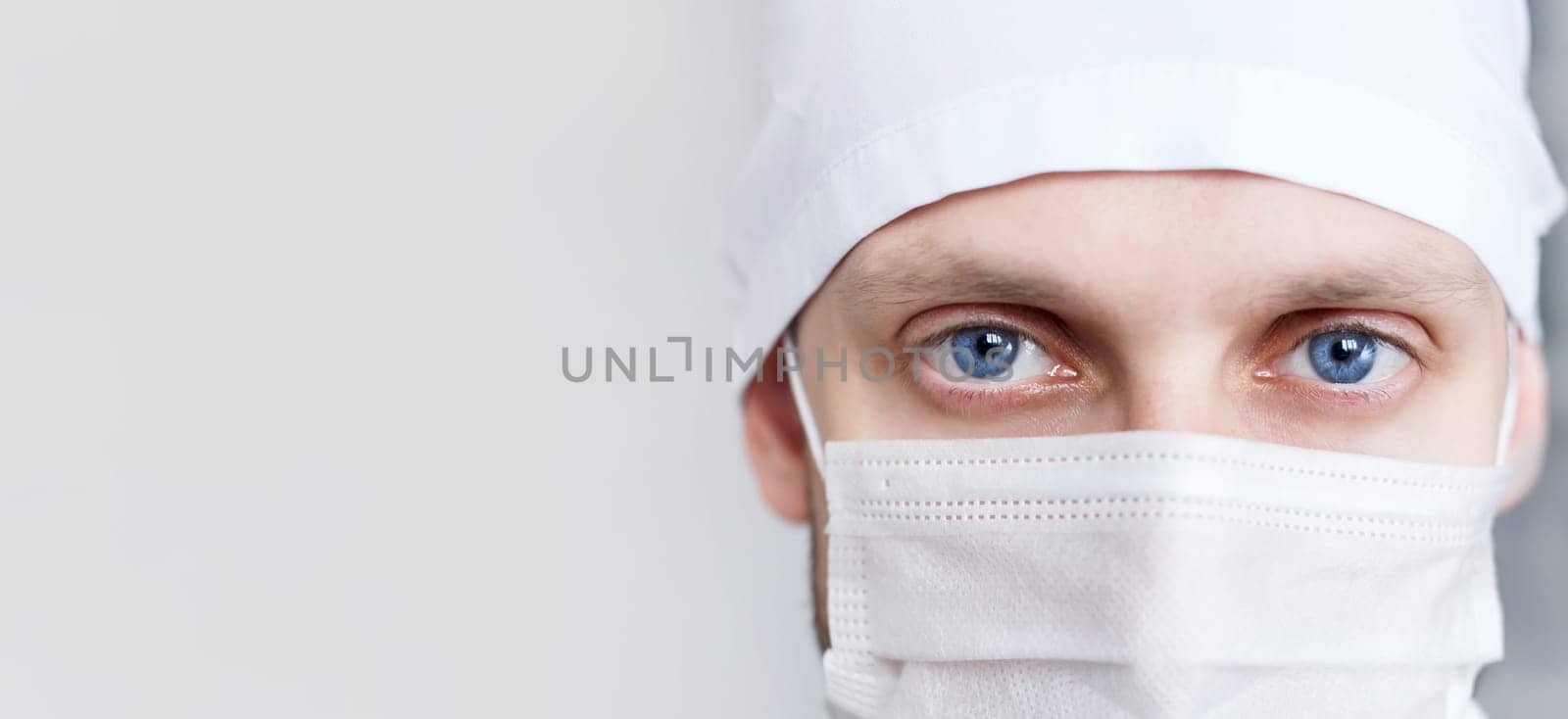 Young man doctor in cap and mask looks at camera, close-up.