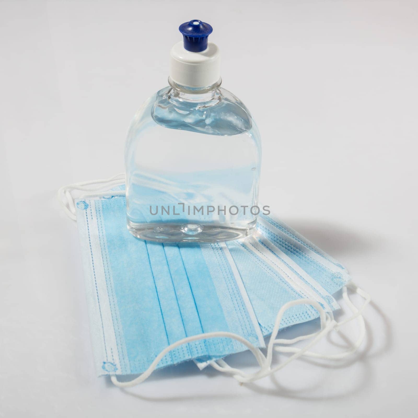 Alcohol gel hand sanitizer and disposable hygienic mask on gray background
