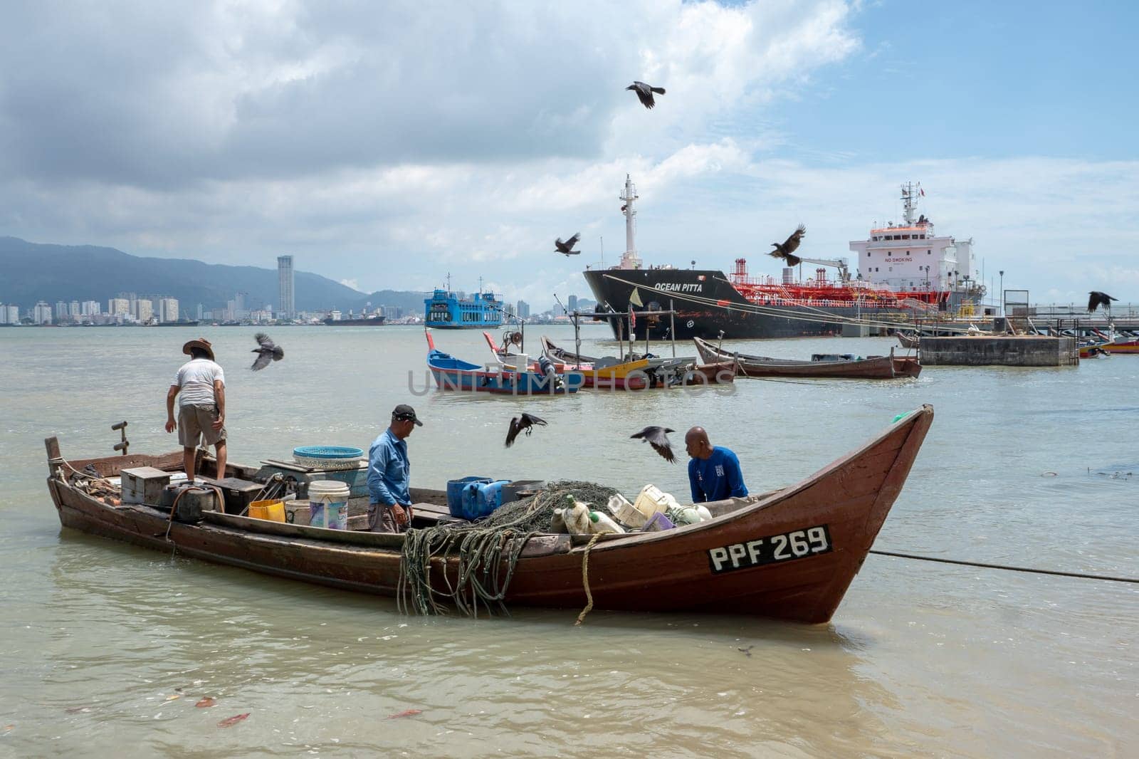 George Town, Penang/Malaysia - Jun 27 2017: Crows fly nearby the fisherman boat. Background is KOMTAR building, ferry, and vessel ship.