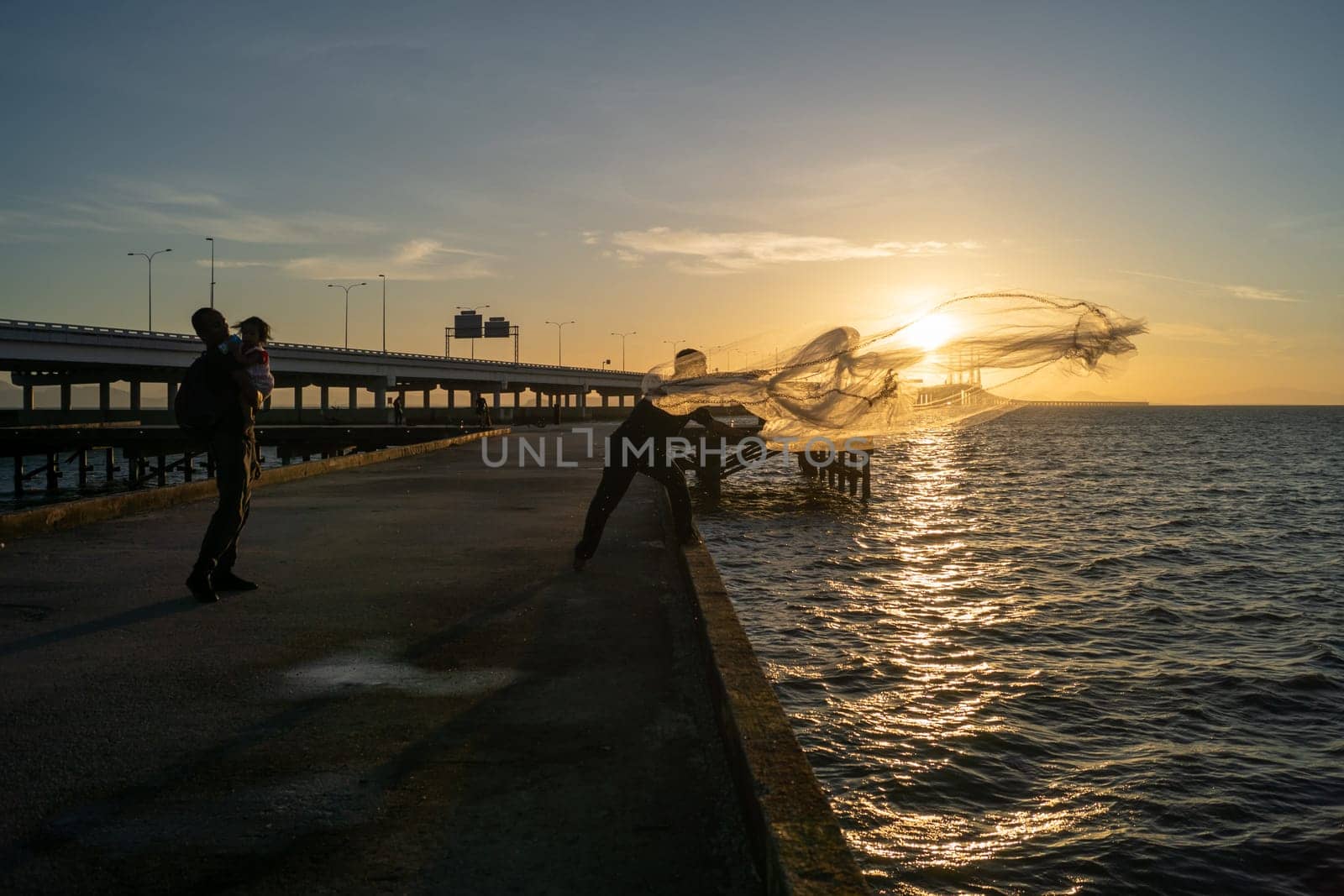 Batu Maung, Penang/Malaysia - Jan 01 2020: A man casting net to sea. Another man hug a child.