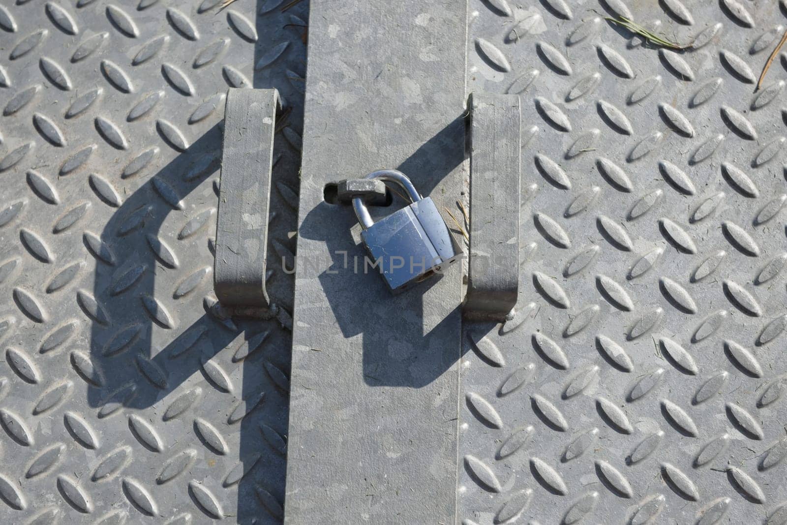 Checkered diamond patterned galvanized steel plates, lit by natural sunlight in an outdoor setting. Shiny metal padlock sits between the two handles