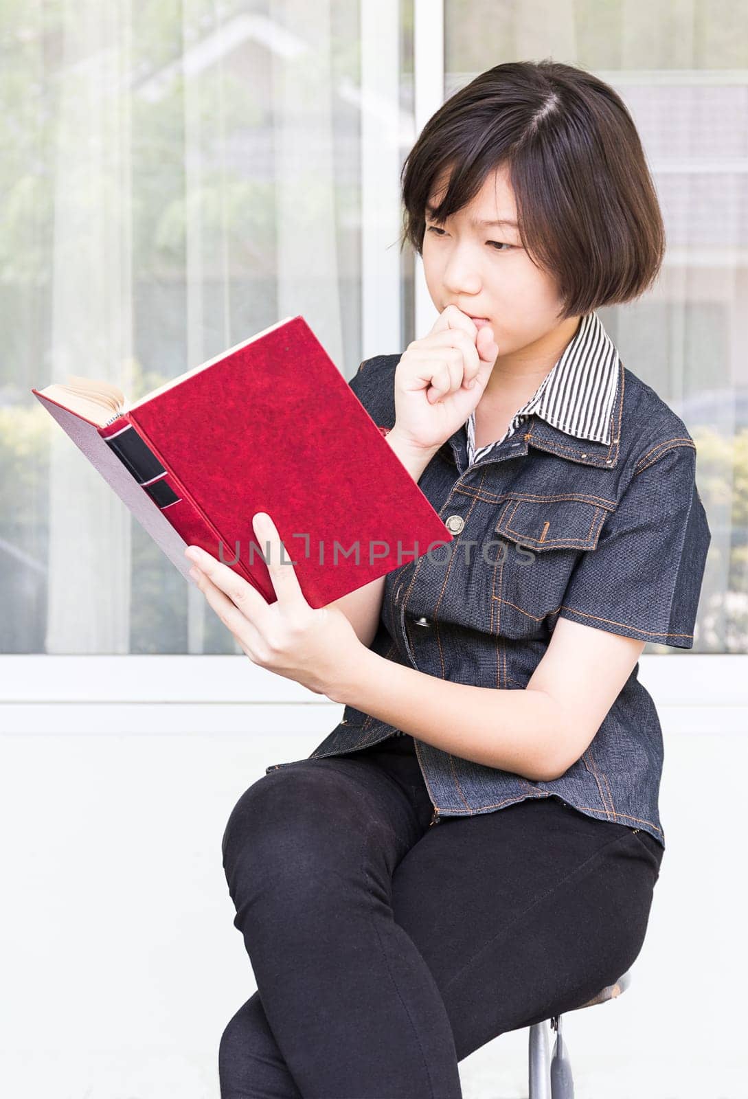 Asian girl with short hair reading a book sitting on a chair