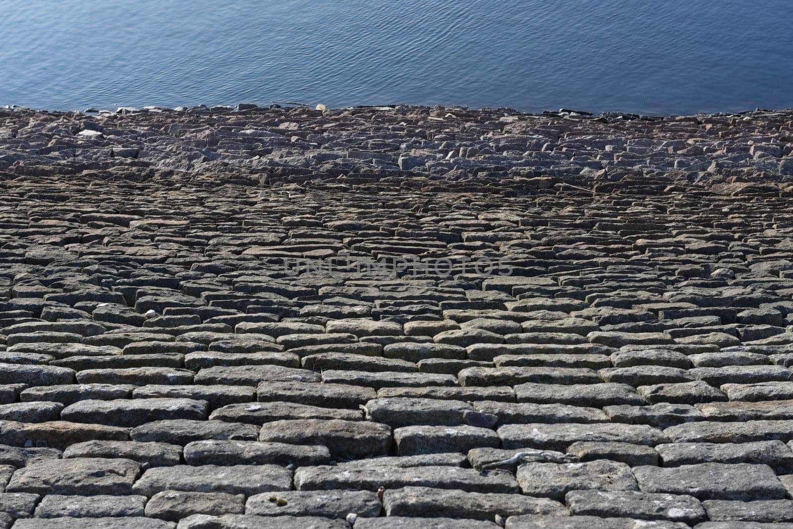Looking down a sloping reservoir stone wall, a full frame abstract texture image is formed. Deep blue water ripples form good copy space.