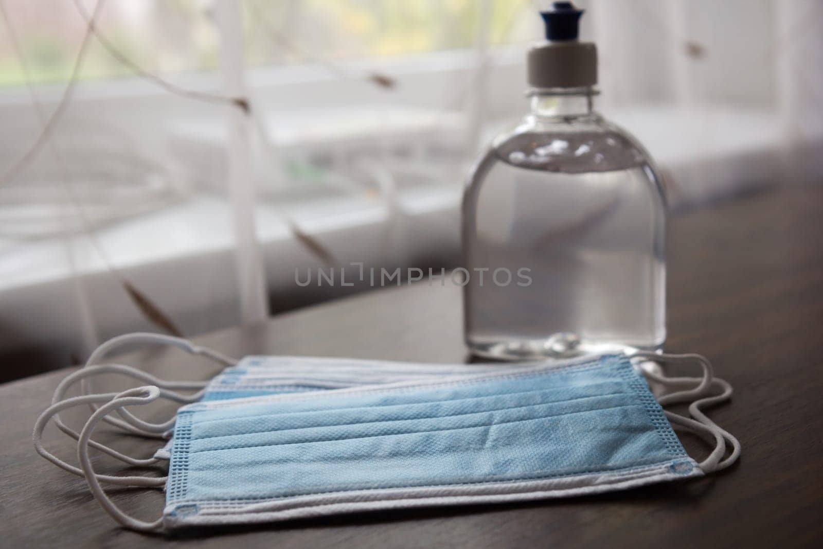 Alcohol gel hand sanitizer and disposable hygienic mask on table