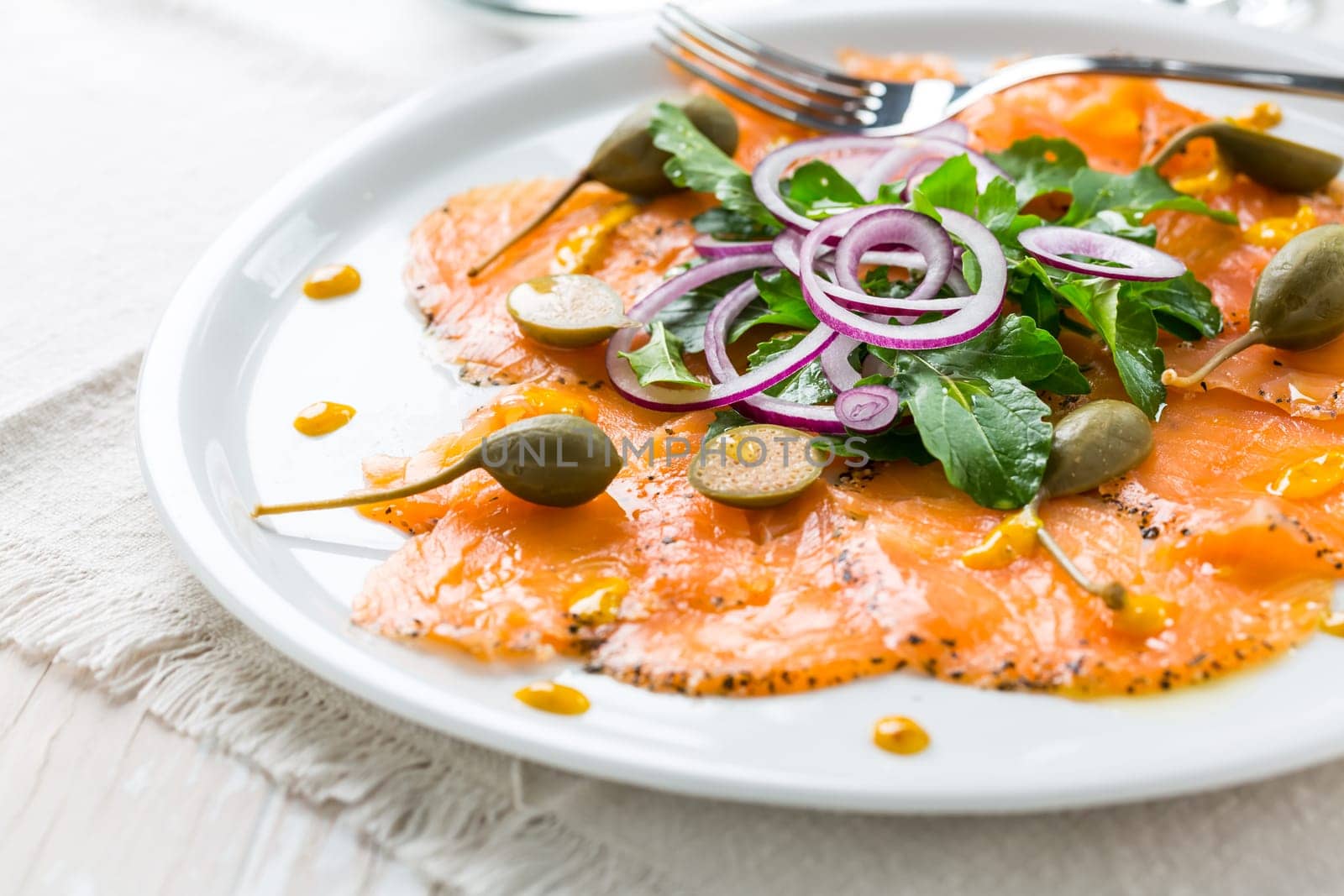 Salmon carpaccio and arugula salad with onions and capers on white plate