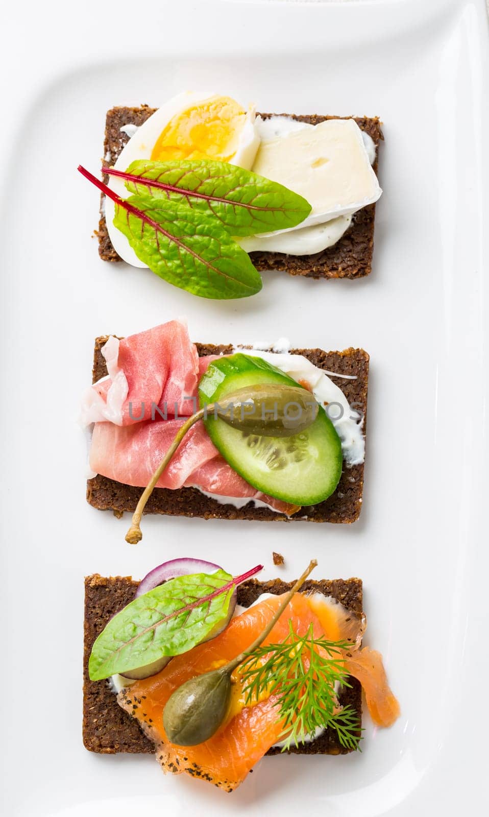 Variation of healthy open sandwiches on Pumpernickel bread with vegetables, salmon, ham, herbs and soft cheese