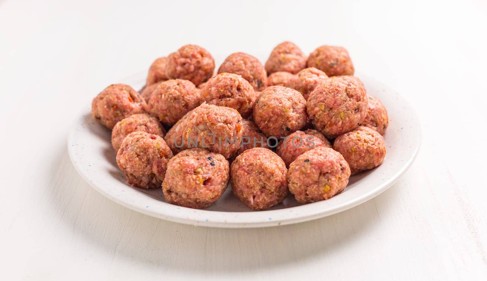 Raw meatballs on plate, ready for cooking or baking on white background