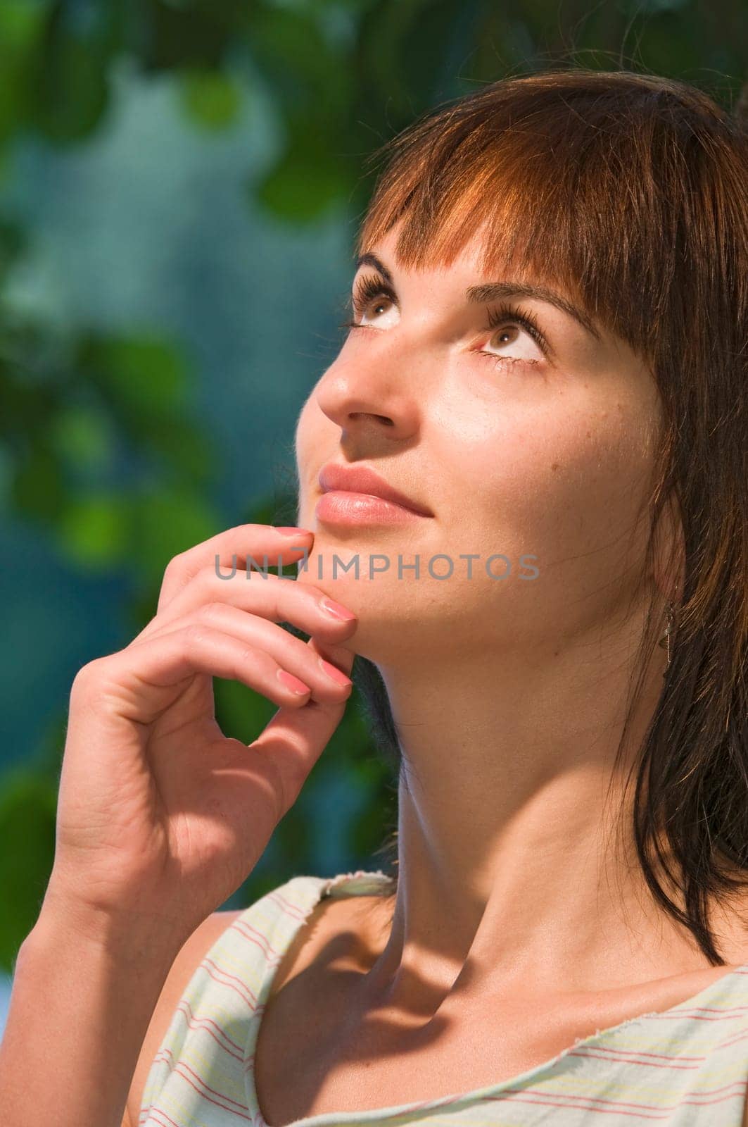 Partial head portrait of a young woman looking up, thoughtfully holding her right hand to her chin.