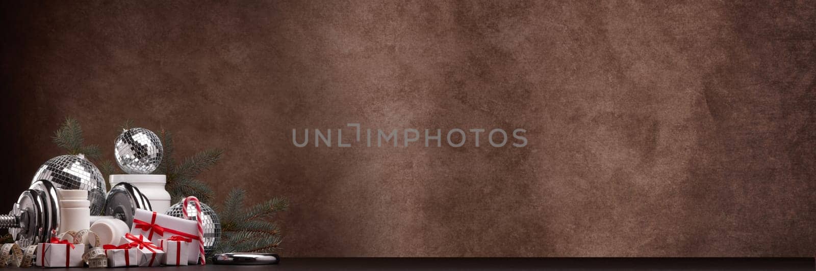 Sports nutrition (supplements), sports equipment, fir branch,  gift boxes, Christmas ornaments on dark brown background with copy space. Fitness, sport, healthy lifestyle concept. New Year. Christmas.