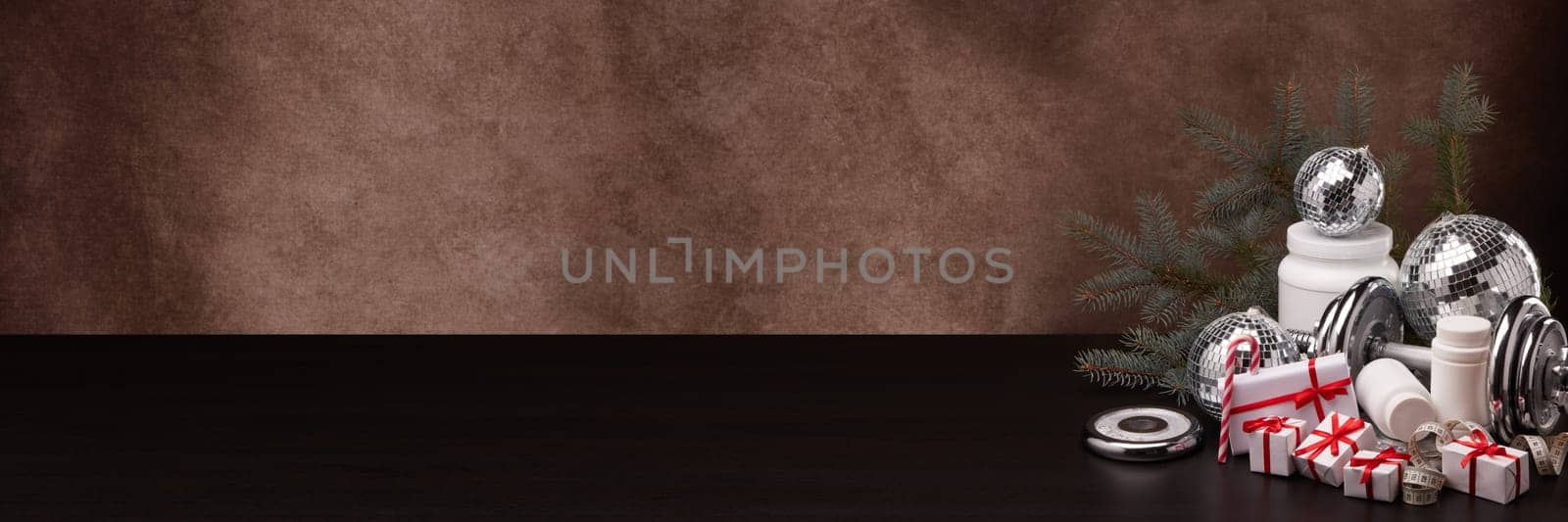 Sports nutrition (supplements), sports equipment, fir branch,  gift boxes, Christmas ornaments on dark brown background with copy space. Fitness, sport, healthy lifestyle concept. New Year. Christmas.