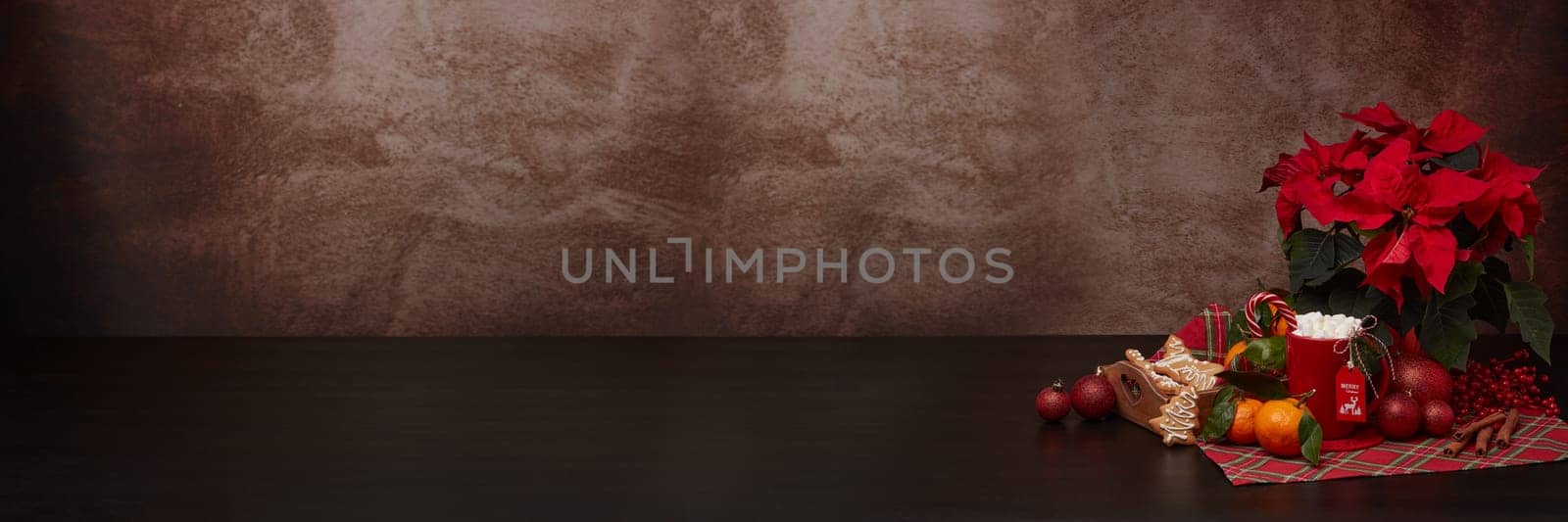 Red Poinsettia flowers, tray with ginger cookies and mandarines, mug with hot cocoa and marshmallows. fir ornaments on brown background with copy space. Winter holidays. New Year, Christmas treat.