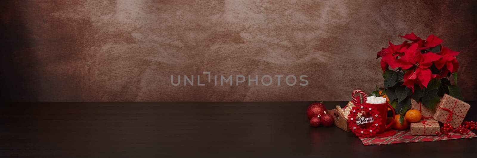Red Poinsettia flowers, tray with ginger cookies, mandarines, mug with hot cocoa and marshmallows. fir ornaments, gifts on brown background with copy space. Winter holidays. New Year, Christmas treat