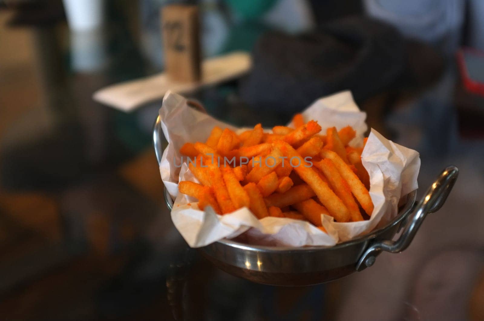 Hand holding French fries with chili cheese powder in a pan