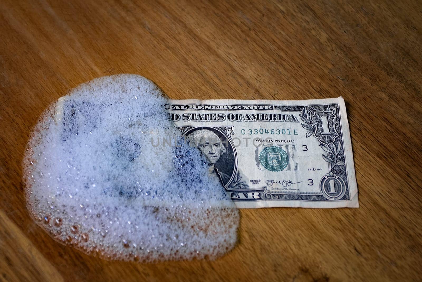 A one dollar bill partially covered by foam on a wooden surface