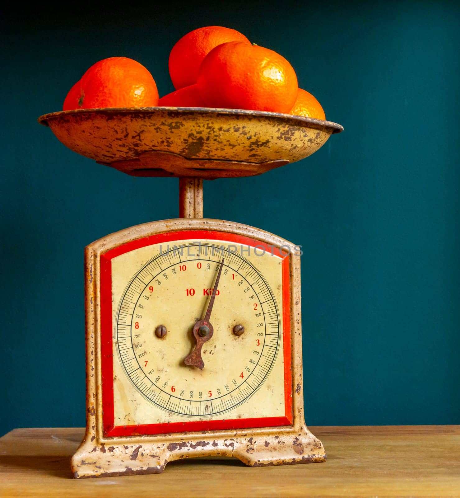 Weighing tangerines in a retro, vintage and worn out scale or balance, on a wooden plank against a guatemala green wall.