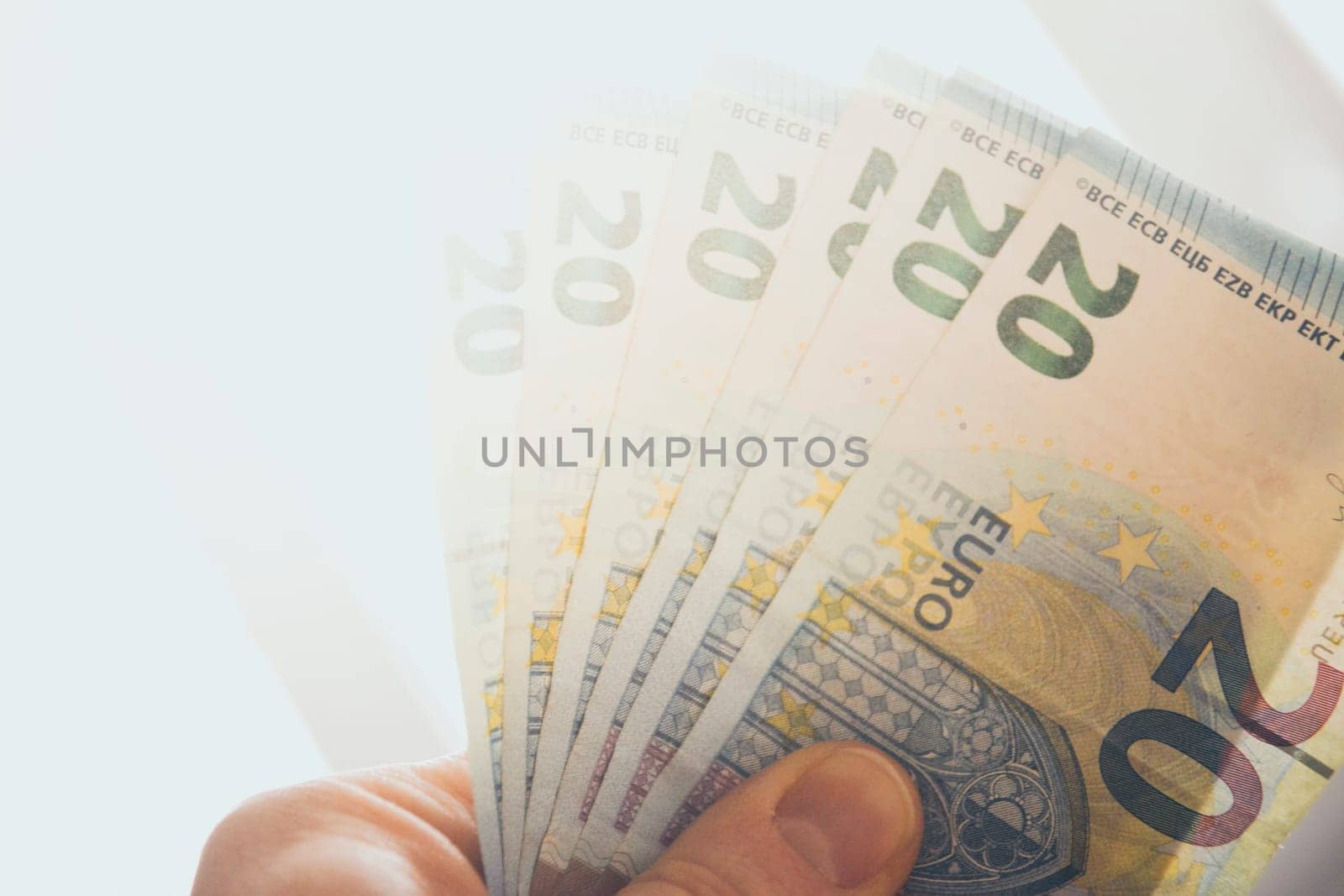 Hand holding spread out 20 euro banknotes against strong sunlight
