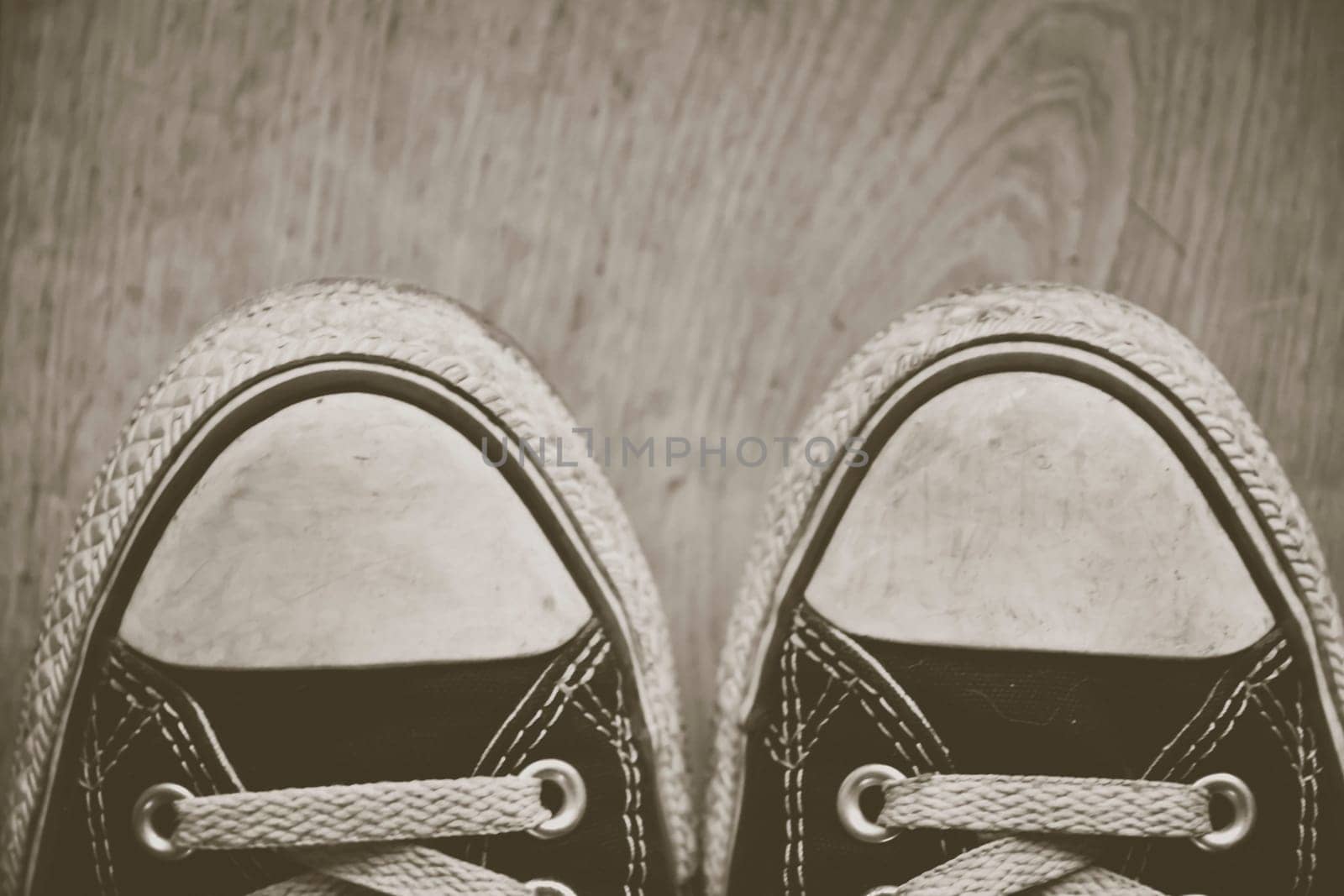 orn out converse Chuck Taylor All-Star sneakers tips, with black fabric, on wooden floor. Creative edit.