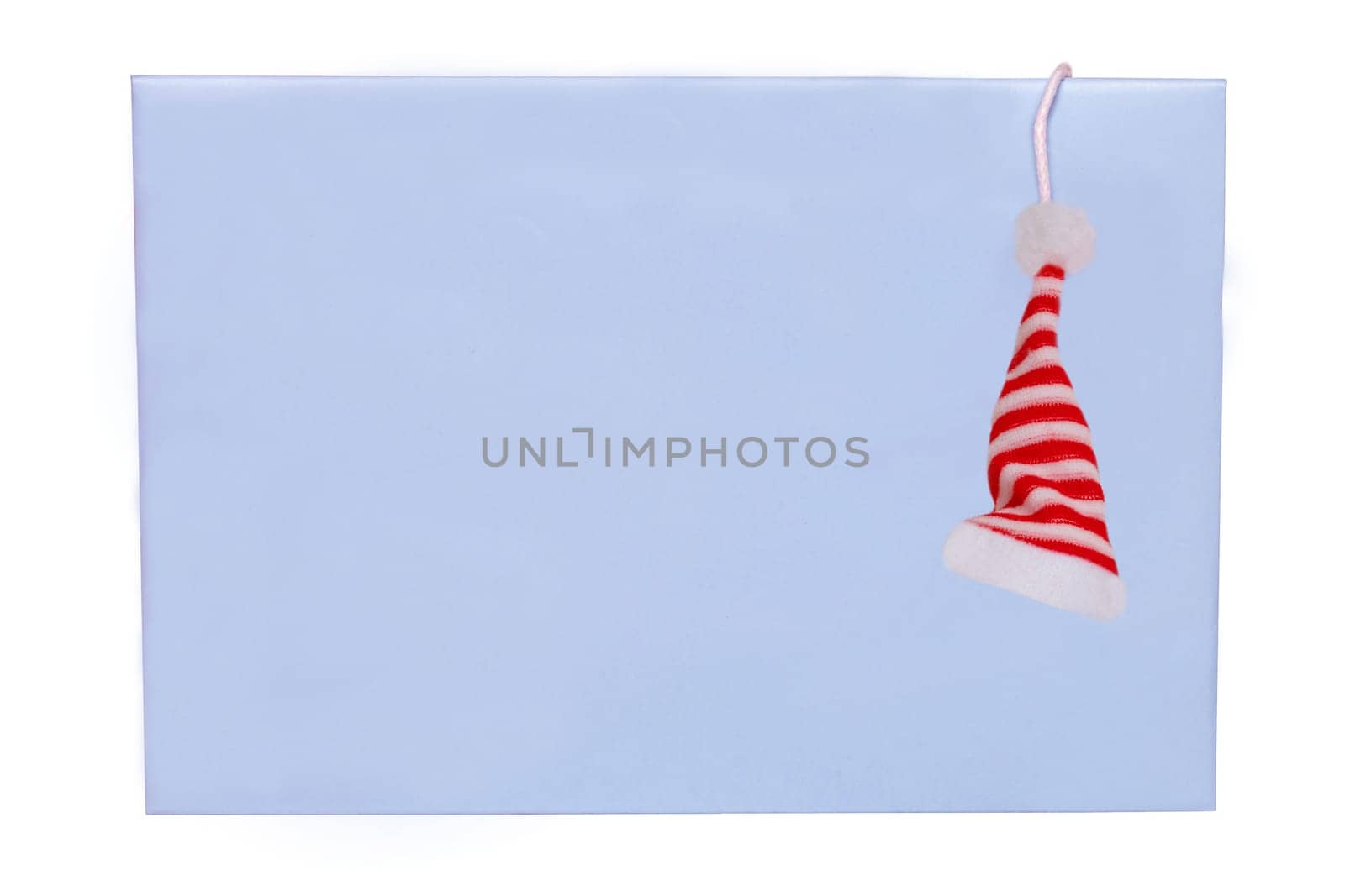 Christmas card template isolated. Closeup of a blue paper envelope with a hanging red Santa Claus hat. Macro.
