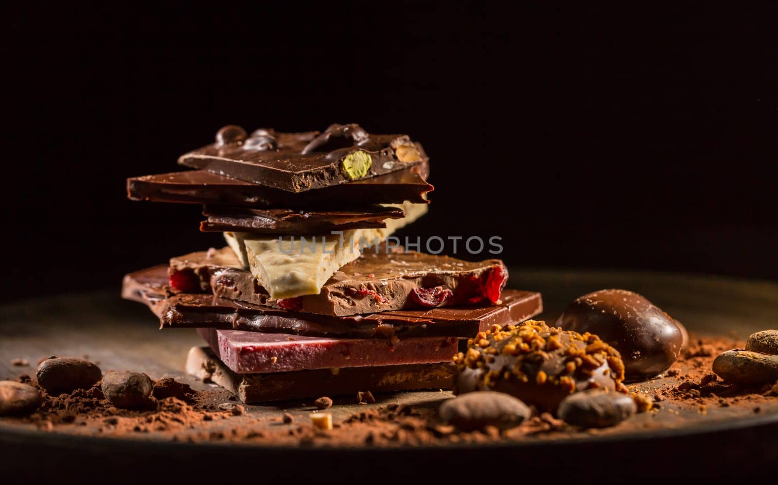 Stack of assorted chocolate with cocoa and cocoa beans on black background