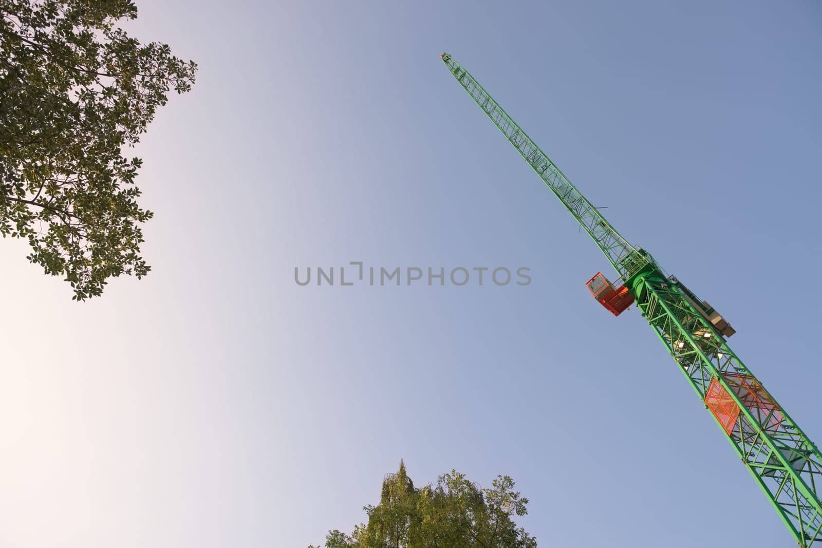Smooth early morning sky background behind the leaves of tree tops and the leading jib of a large tower crane. Abstract with plenty of copy space.