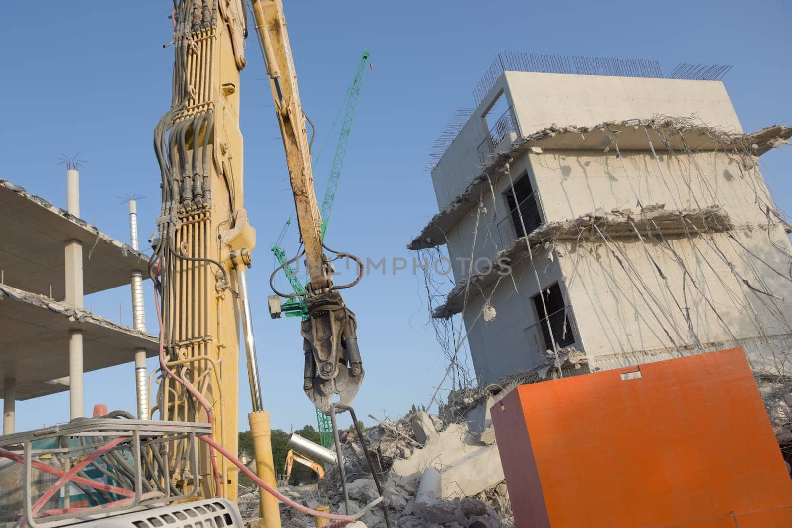 Concrete rubble and hanging steel cables on this demolition site, Large high reach demolition excavator in the foreground, with tower crane behind