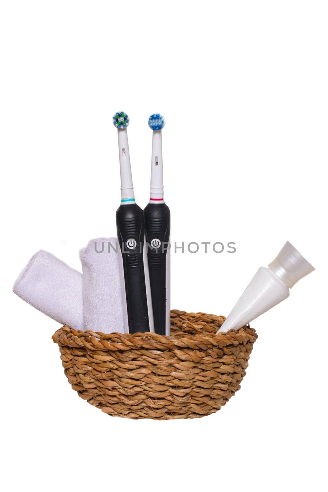 Two electrical tooth brushes, an oral care product or toothpaste and towels in a basket isolated on a white background. Dental and healthcare concept. Copy space.