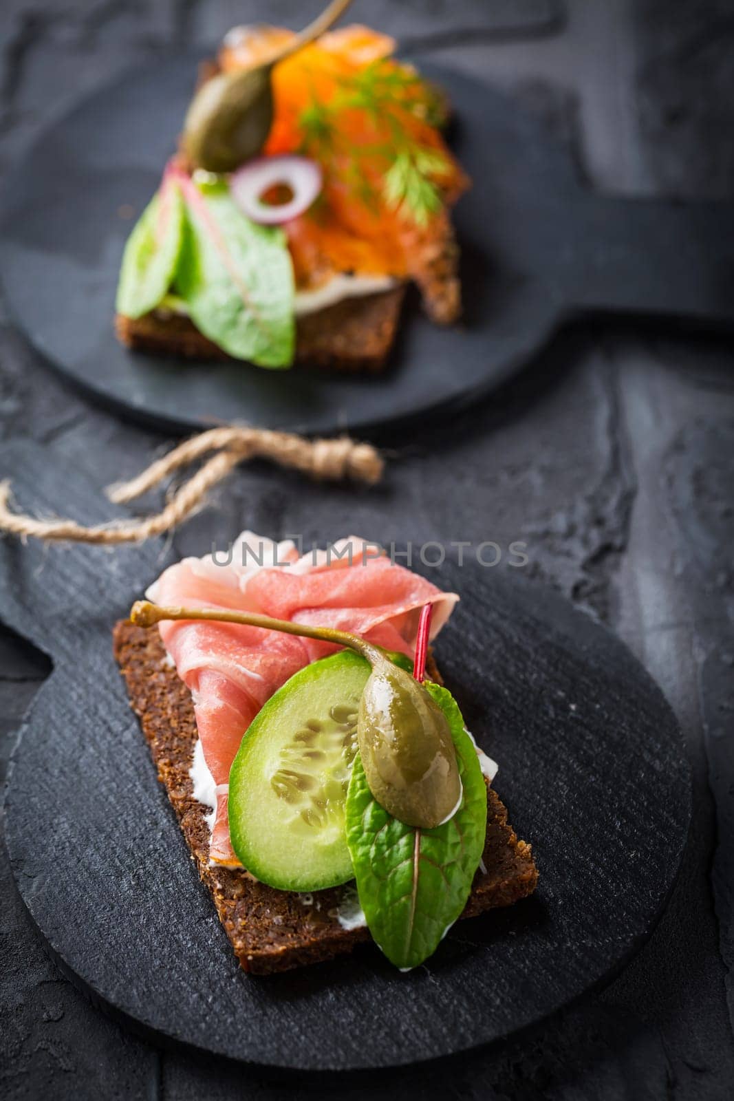 Variation of healthy open sandwiches on Pumpernickel bread with vegetables, salmon, ham, herbs and soft cheese
