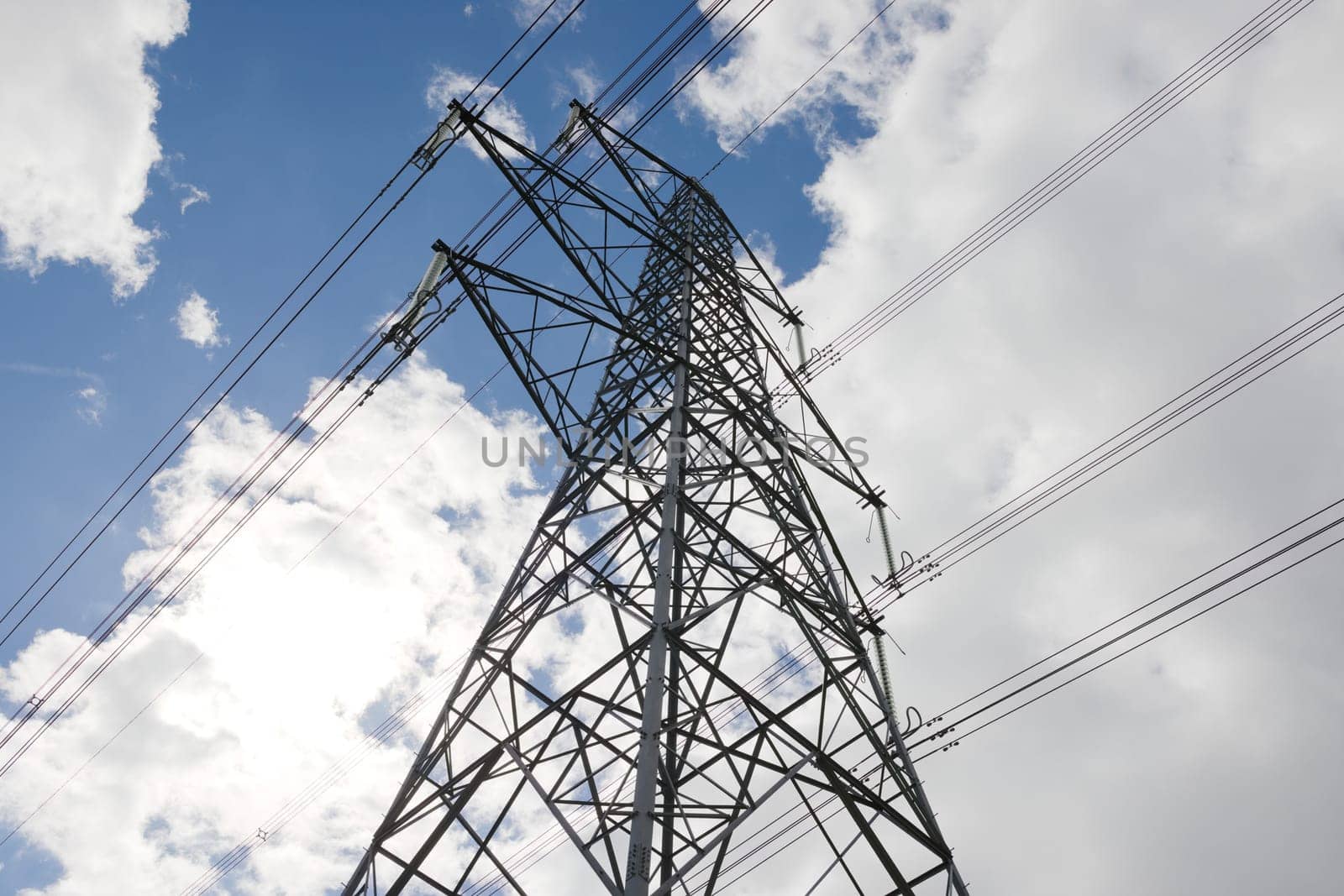 Low angle image of an electrical transmission lattice tower. High voltage power lines silhouetted against the summertime sky. Spacers hang from tower