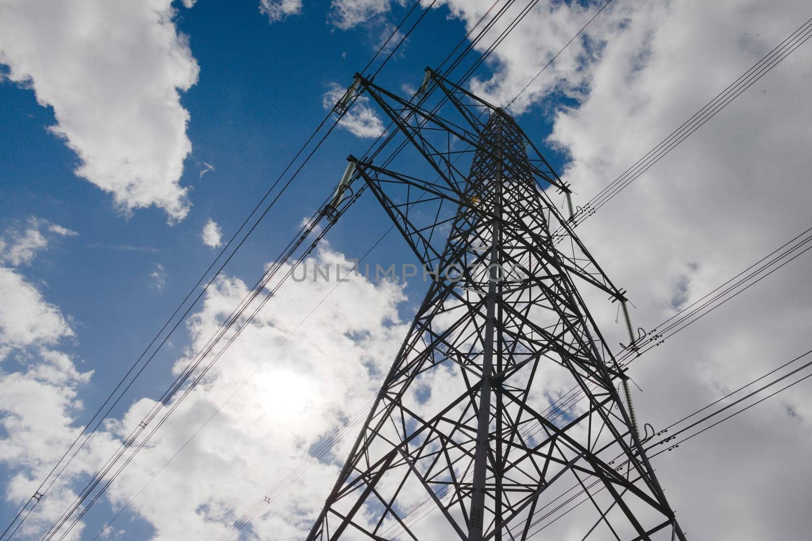 Environmental contrasts, big dark metal electrical pylon against a natural cloudy blue sky. Copy space to left hand side, bright sunlight
