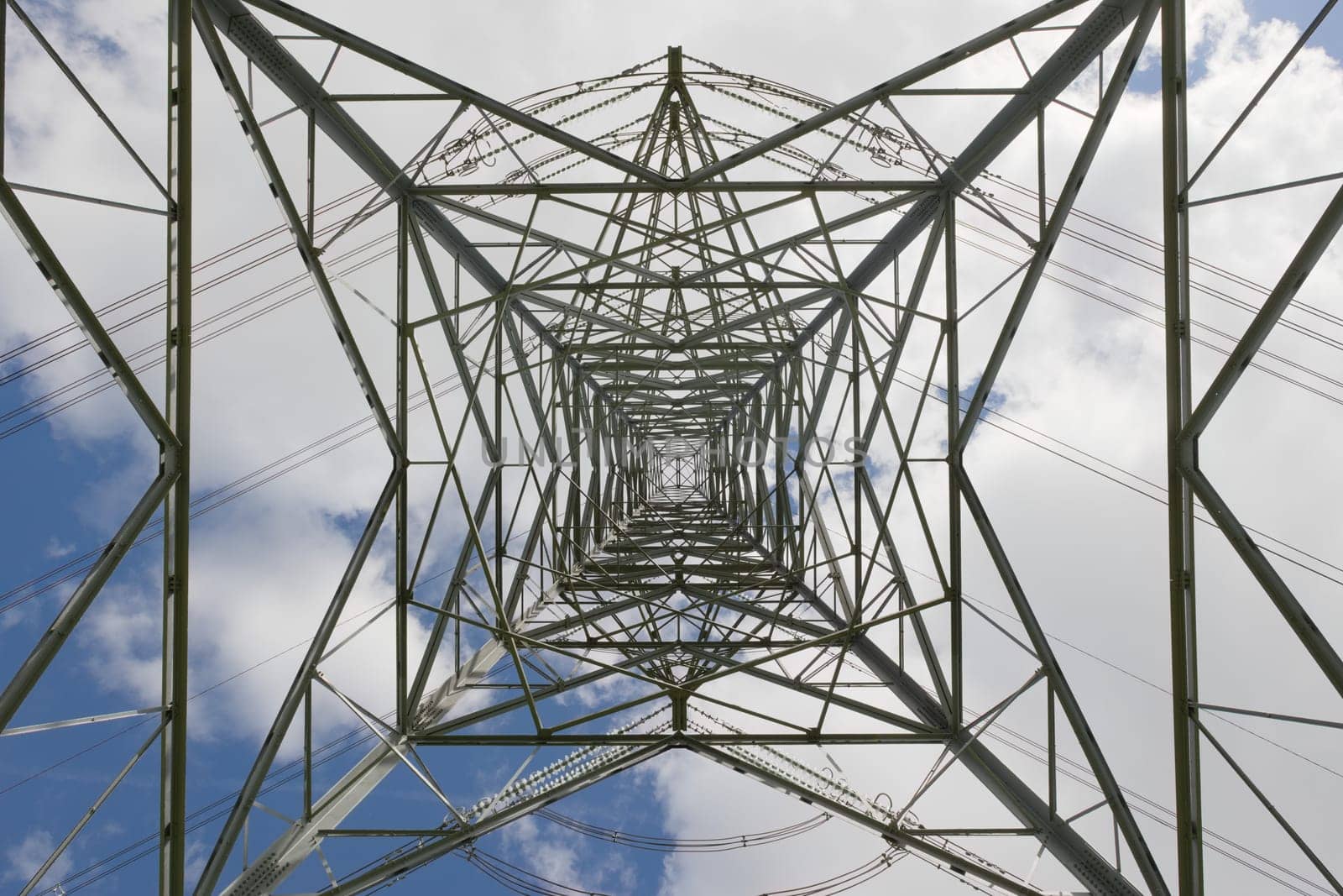 Industrial electrical transmission lines and pylon tower. Repeating, converging and intricate patterns are created by the metal lattice structure.