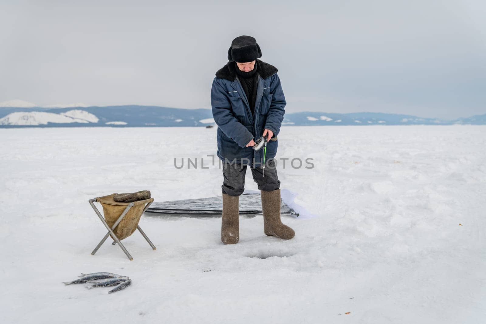 Baikal lake, Siberia, Russia - March 05, 2020 : Winter ice fishing. A fisherman is fishing on spinings near tents and cars on Lake Baikal on a March day. Baikal lake, Siberia, Russia-96