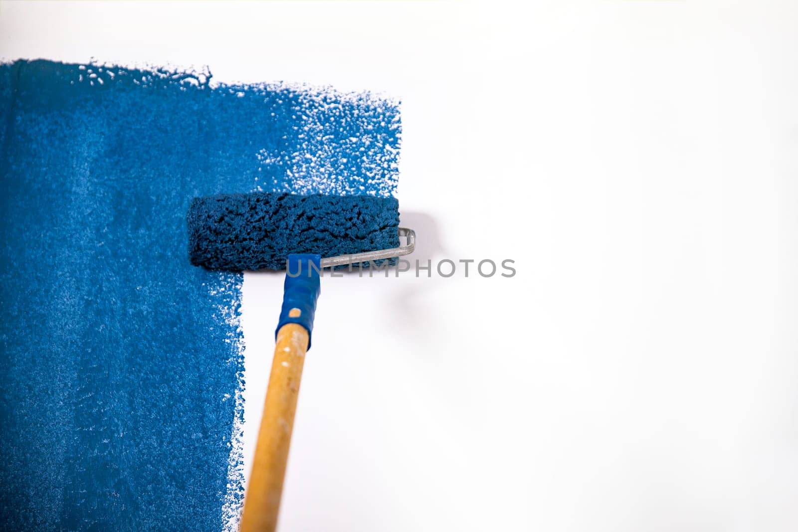 Paintign the wall in blue with roller brush.