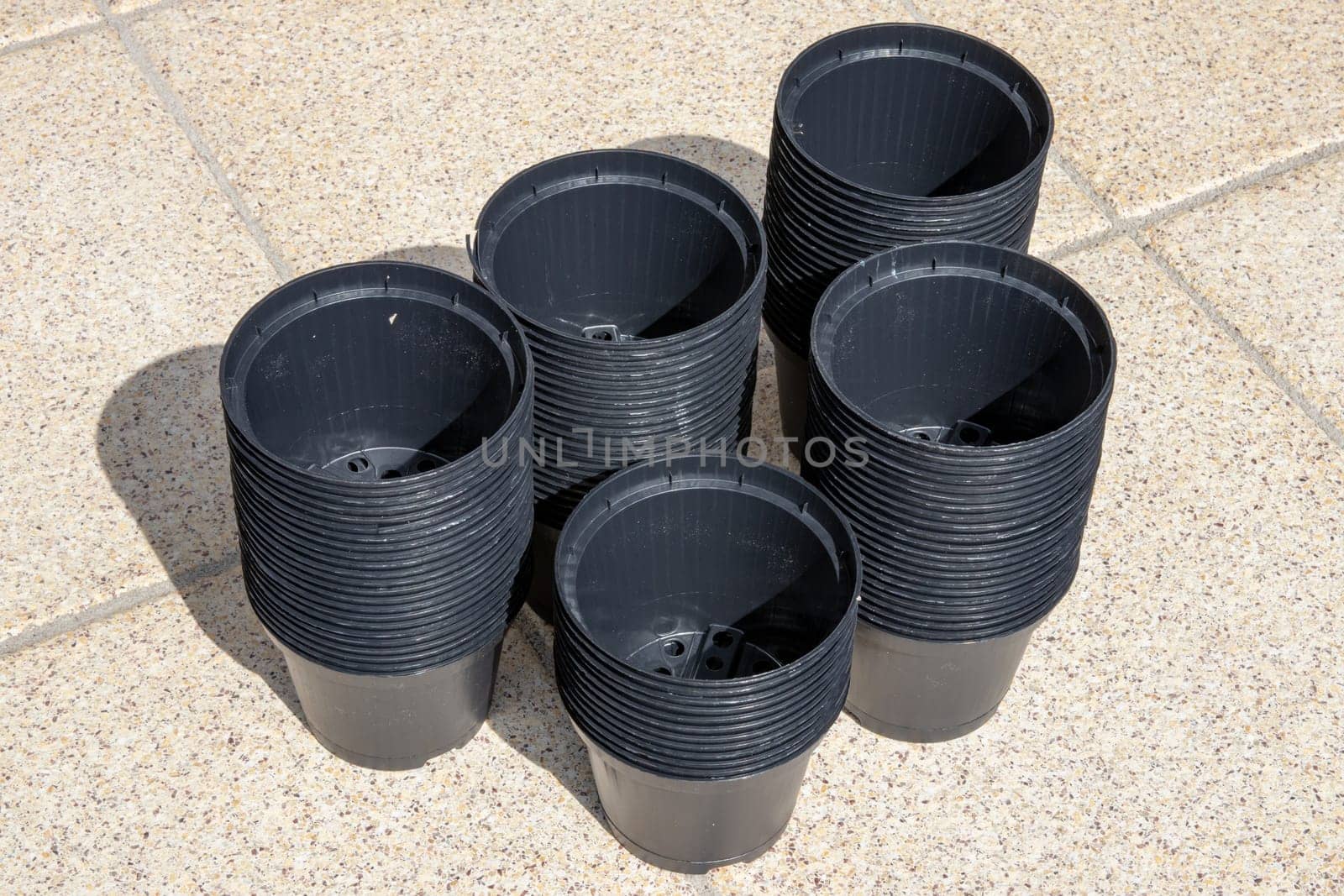 Closeup of empty black plastic plant pots stacked on the terrace on a sunny day. Equipment of the gardener for planting out seedlings.