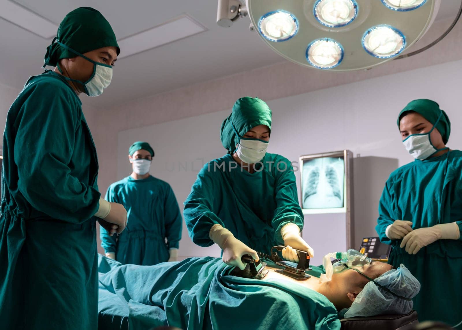 Surgeon doctor and nurse using Defibrillator to patient while patient have problem with Sudden Cardiac Arrest while surgery in Operating Room OR. Medical health care Surgery concept.