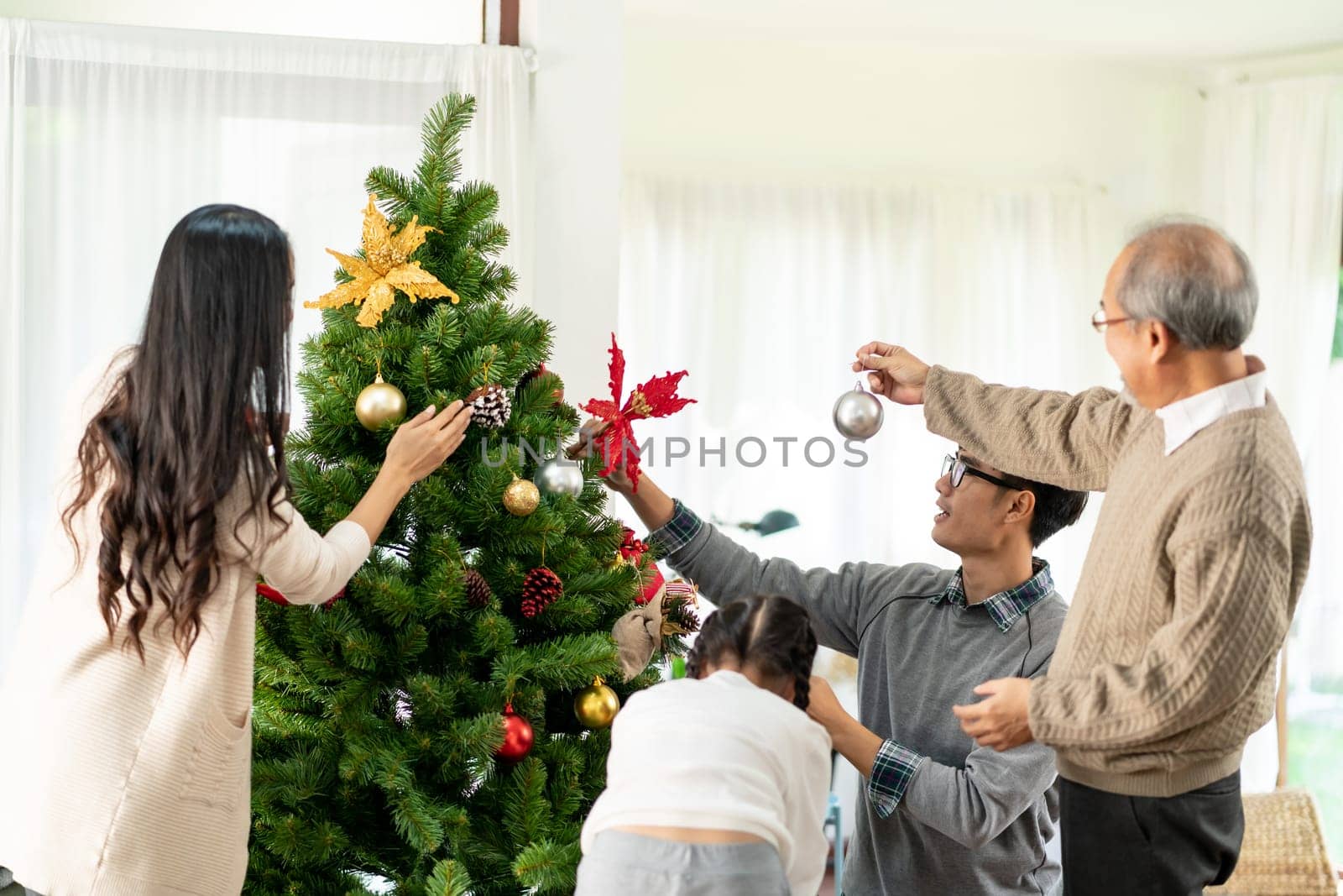 Multigenerational asian Family decorating a Christmas tree. Mom Dad daughter girl and grandfather decorate the Christmas tree prepare for season greeting of Merry Christmas and Happy Holidays.