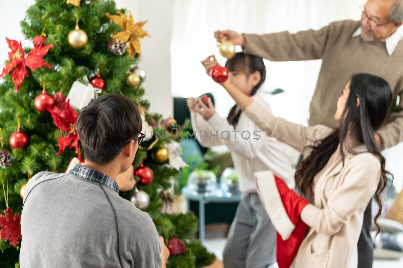 Multigenerational asian Family decorating a Christmas tree. Mom Dad daughter girl and grandfather decorate the Christmas tree prepare for season greeting of Merry Christmas and Happy Holidays.