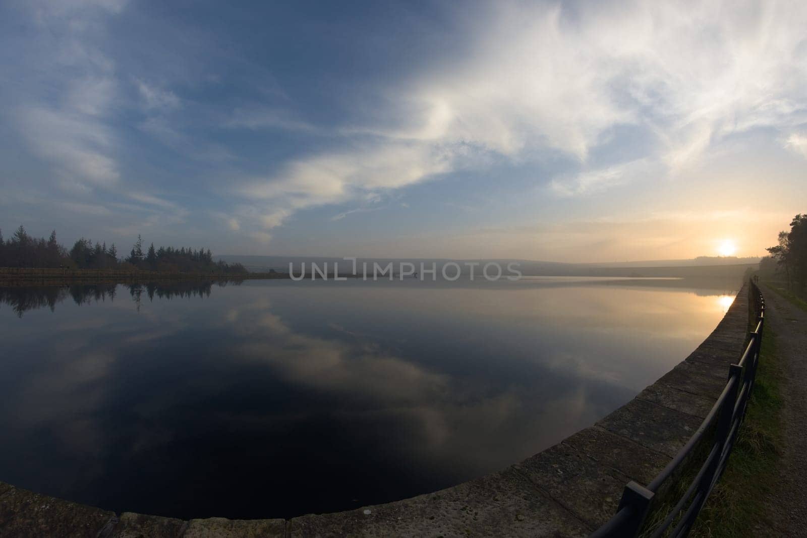 Middle reservoir at redmires reservoirs near sheffield, flat calm at sunset. Fish eye perspective as the water reflects the sunset sky of wispy clouds