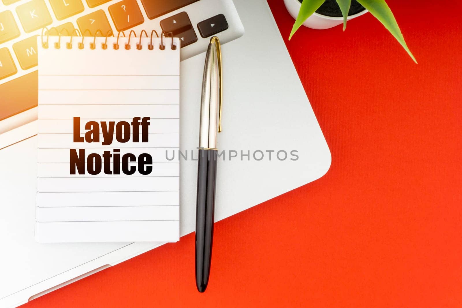 LAYOFF NOTICE text with notepad, laptop, fountain pen and decorative plant on red background. Business and Copy Space Concept