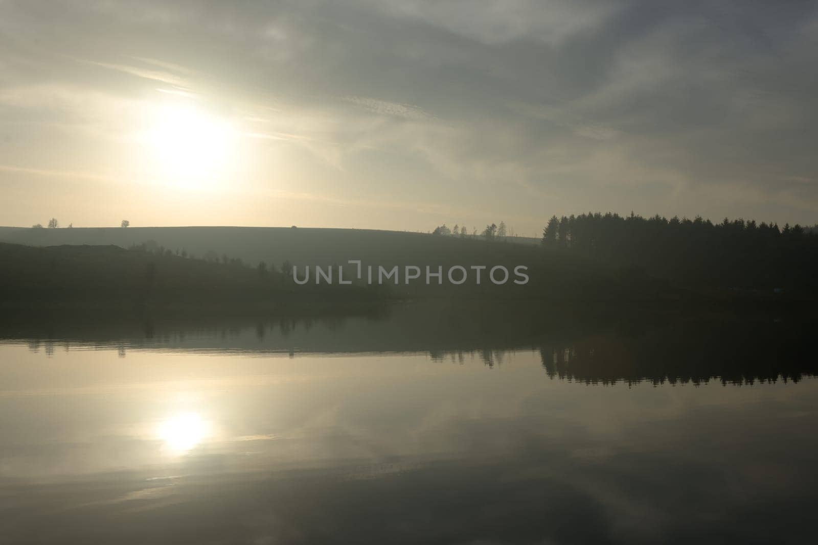 Warm dusky sunset reflected in finely rippled reservoir water at redmires reservoirs near sheffield. Stunning reflected landscape image. Wispy clouds