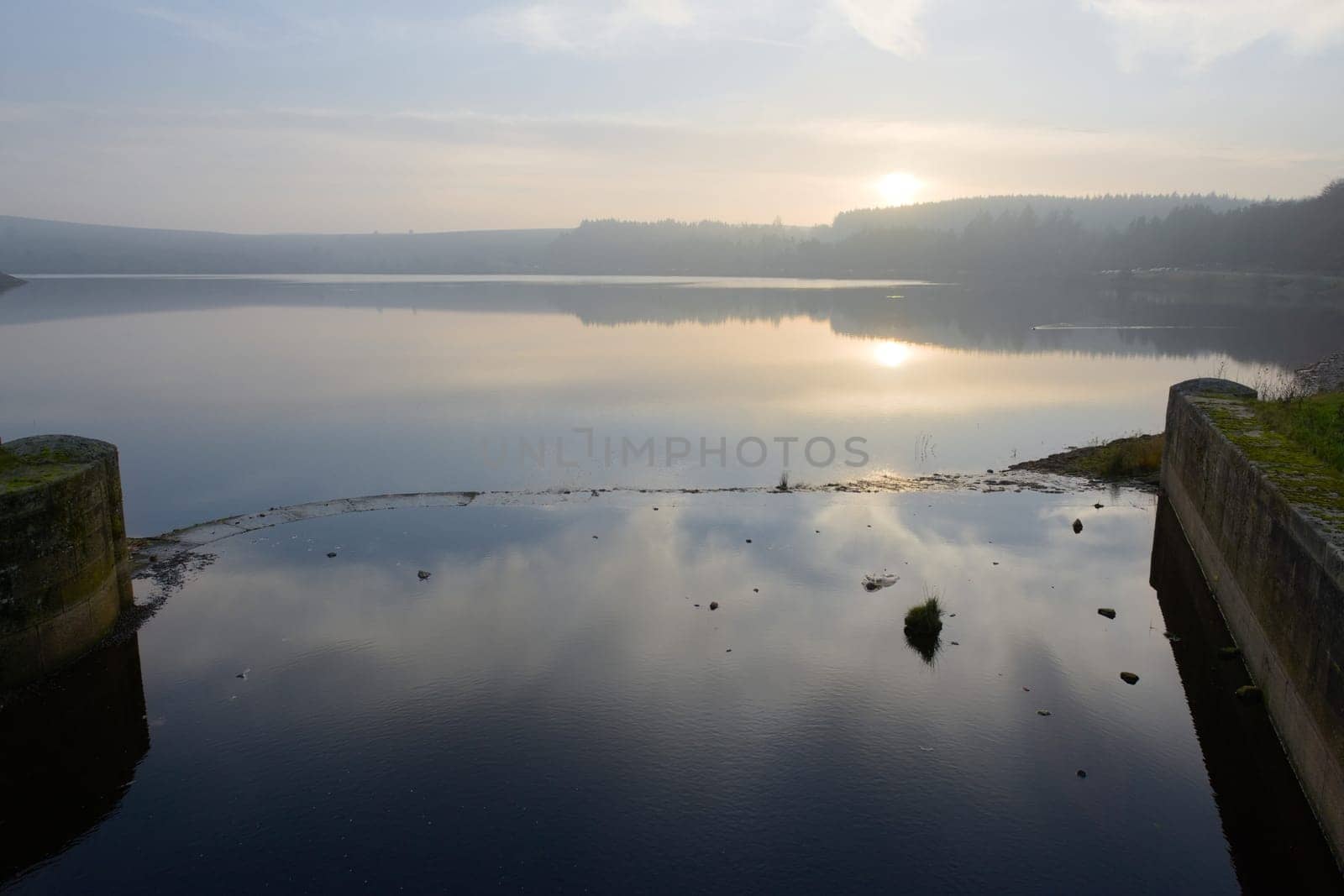 Calm background horizontal landscape image of a sunset reflected in a reservoir near sheffield. Brick walls of reservoir inlet in the foreground.